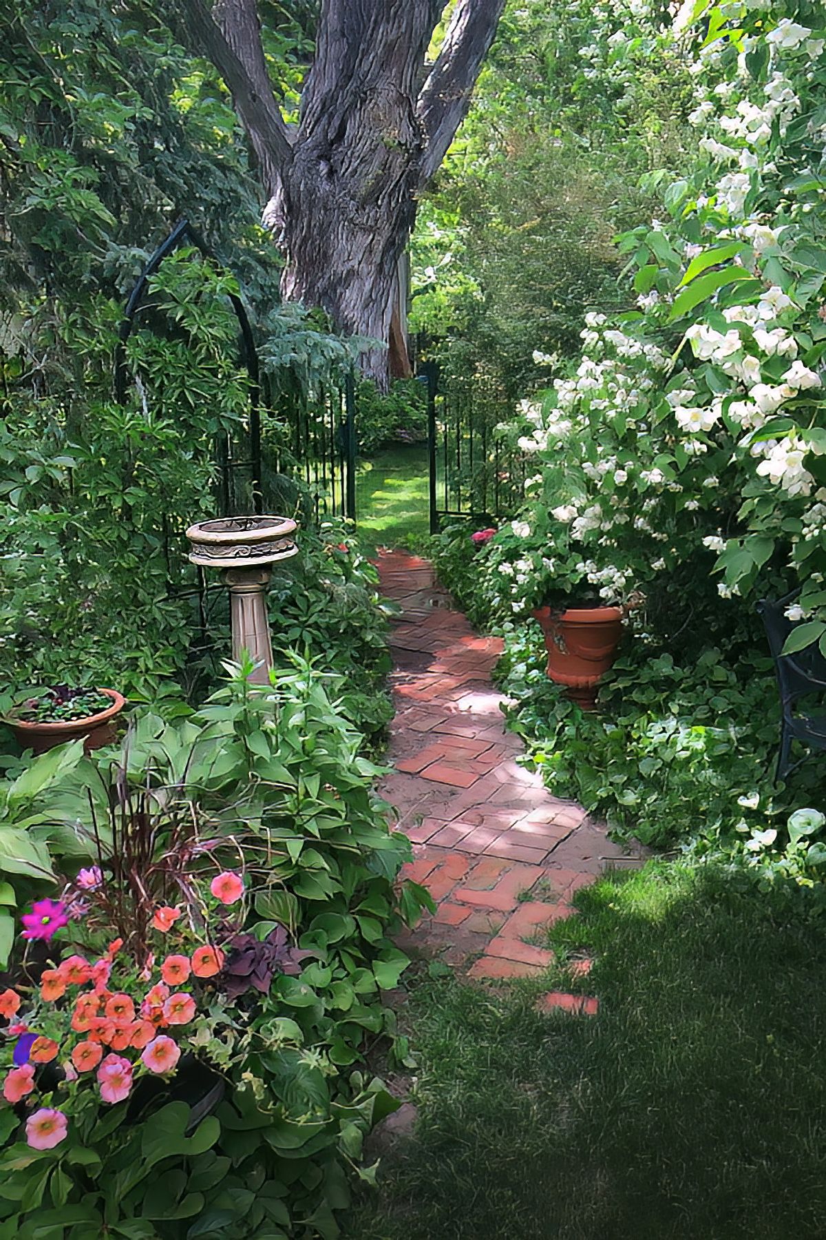 A brick path in a garden surrounded by trees and flowers.