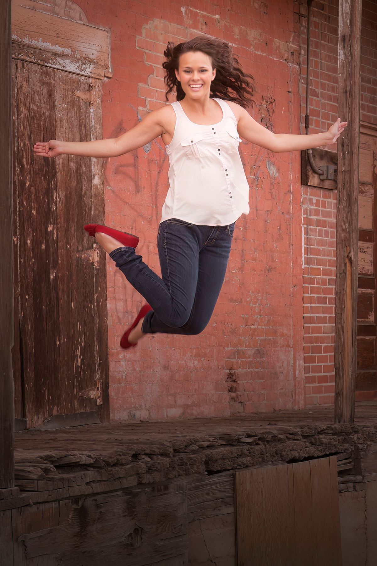 A woman is jumping in the air in front of a brick wall.