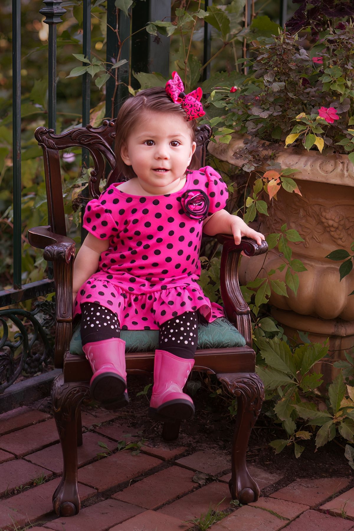 A little girl in a pink polka dot dress is sitting in a chair.