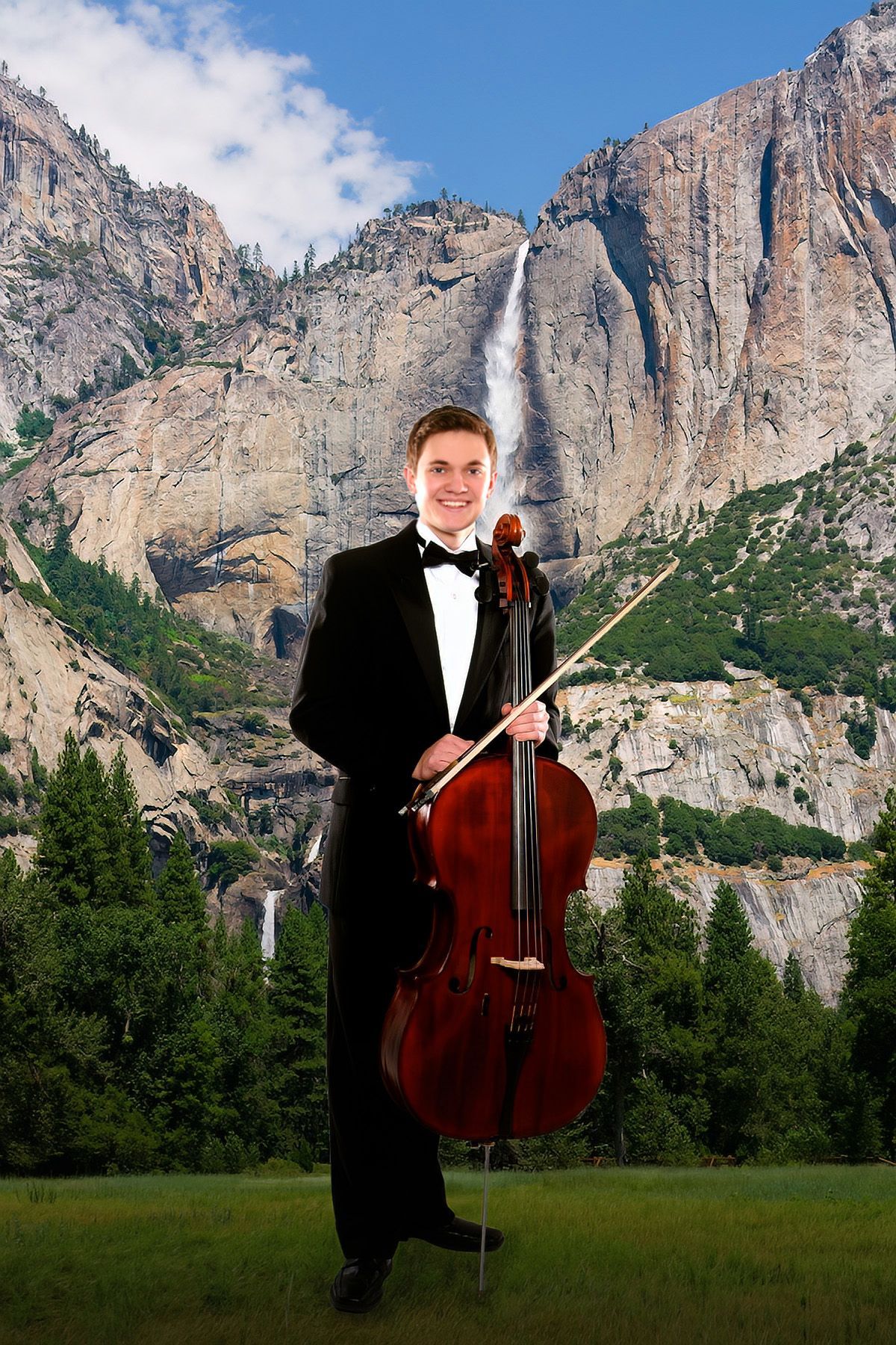 A man in a tuxedo is holding a cello in front of a waterfall.
