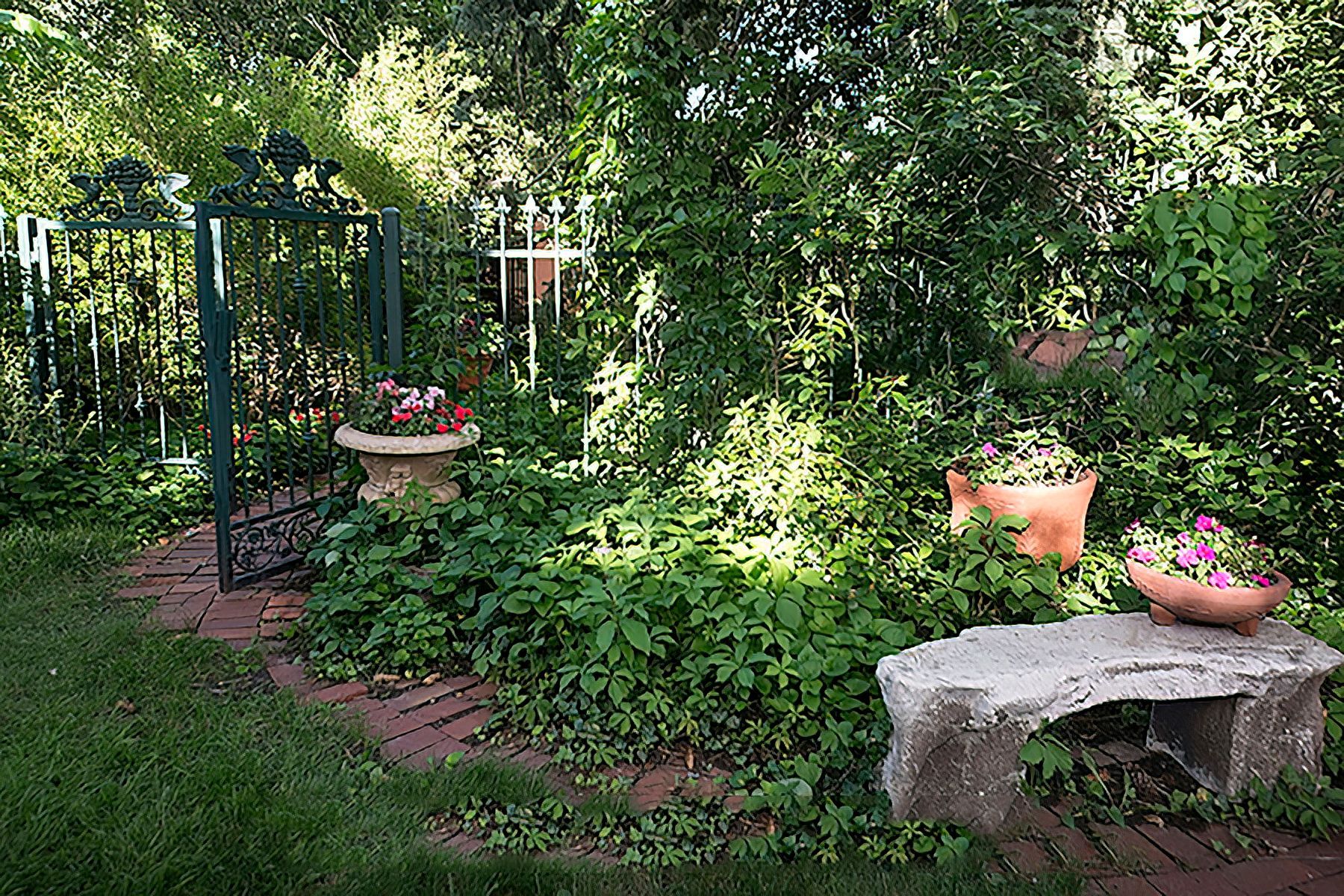 A garden with a stone bench , potted plants and a gate.