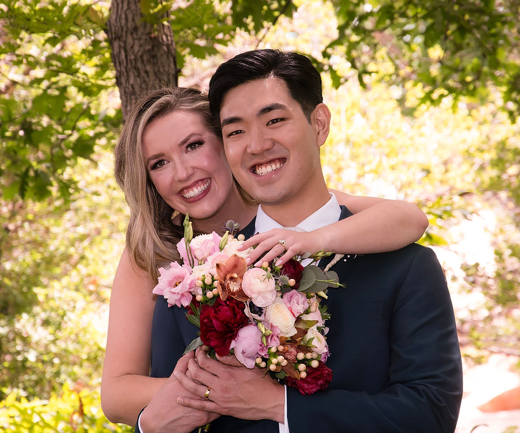 A bride and groom are posing for a picture while the bride is holding a bouquet of flowers.
