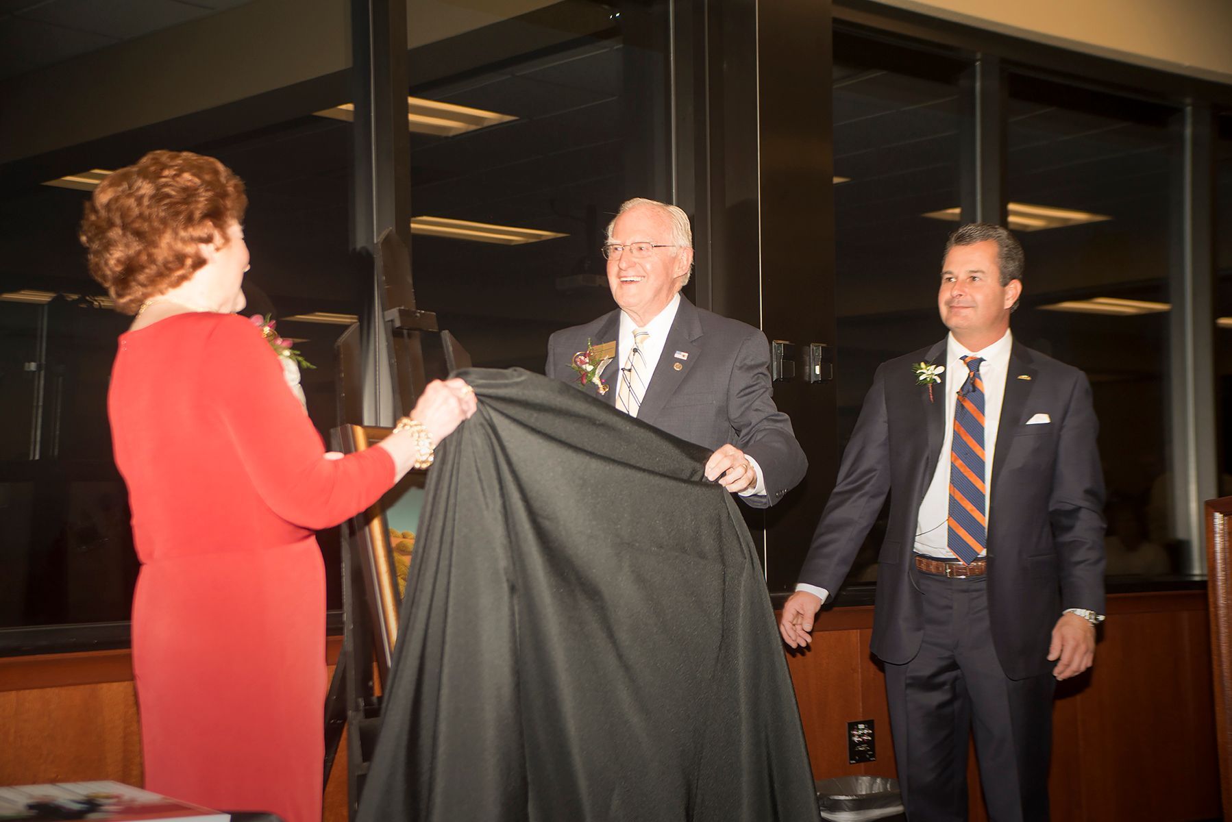 A woman in a red dress is holding a black cloth in front of two men in suits.
