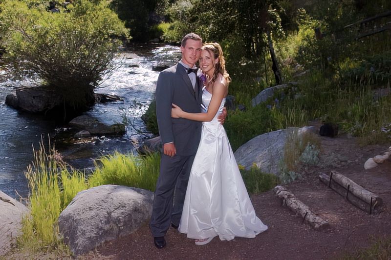 A bride and groom are posing for a picture in front of a river.