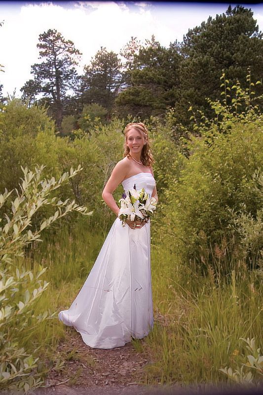 A woman in a wedding dress is standing in a field holding a bouquet of flowers.