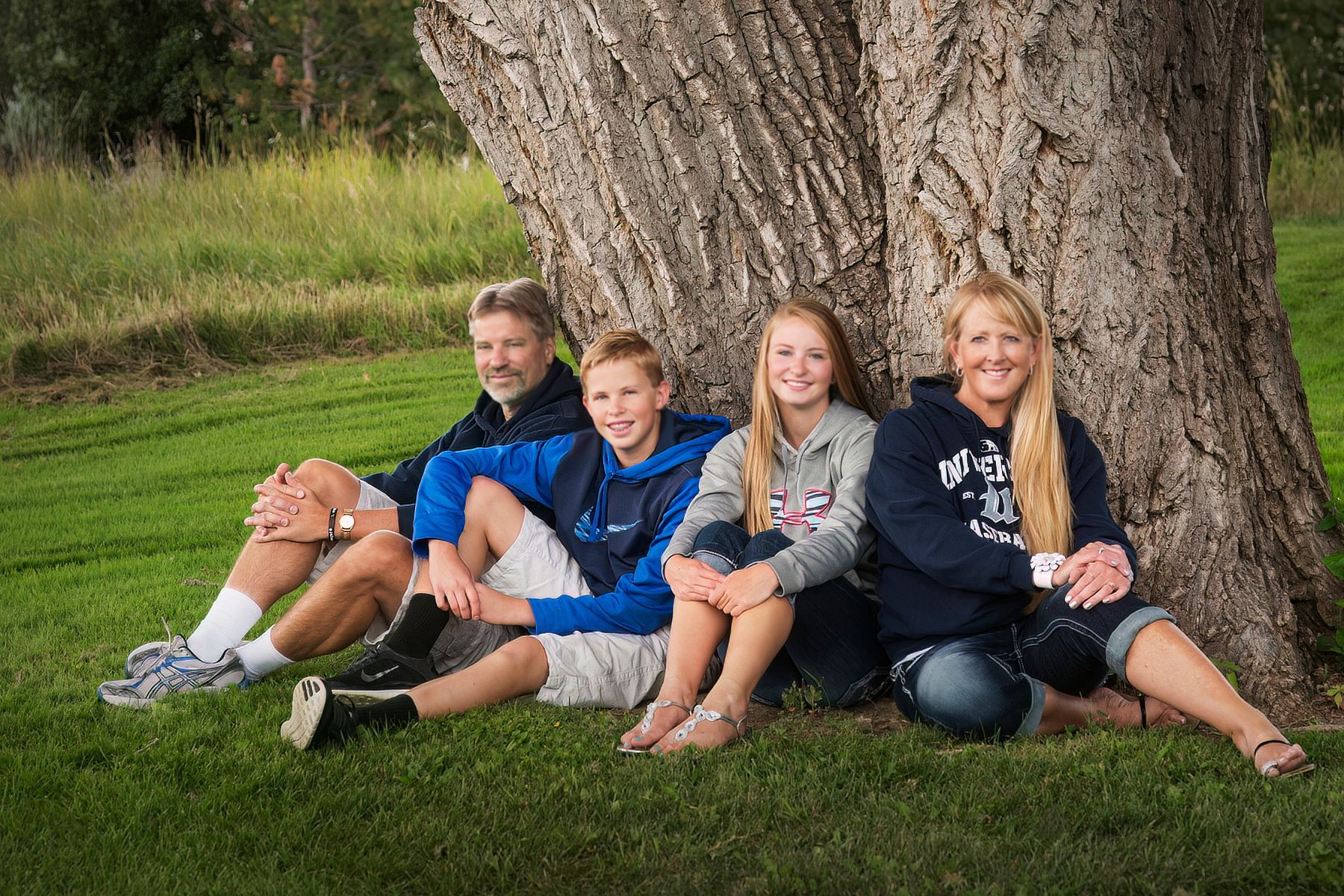 A family is sitting under a tree in the grass.