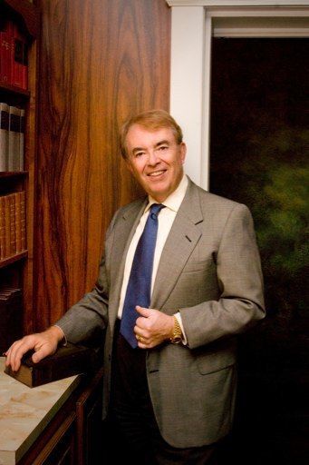 A man in a suit and tie is standing in front of a bookshelf.