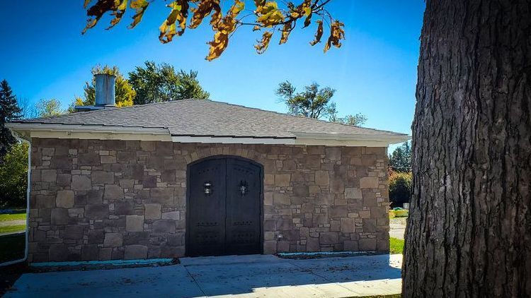 A crematory with a black door and a tree in front of it.