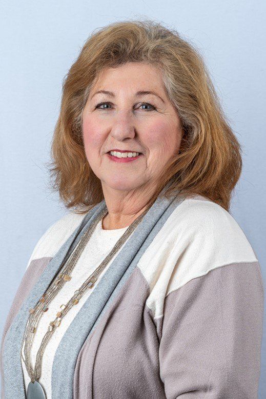 A woman wearing a sweater and a necklace is smiling for the camera.