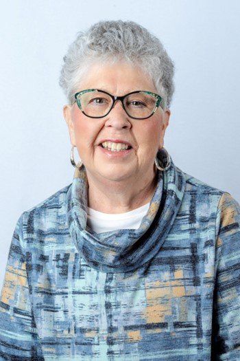 A woman wearing glasses and a blue sweater is smiling for the camera.