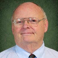 A bald man wearing glasses and a tie is smiling for the camera.