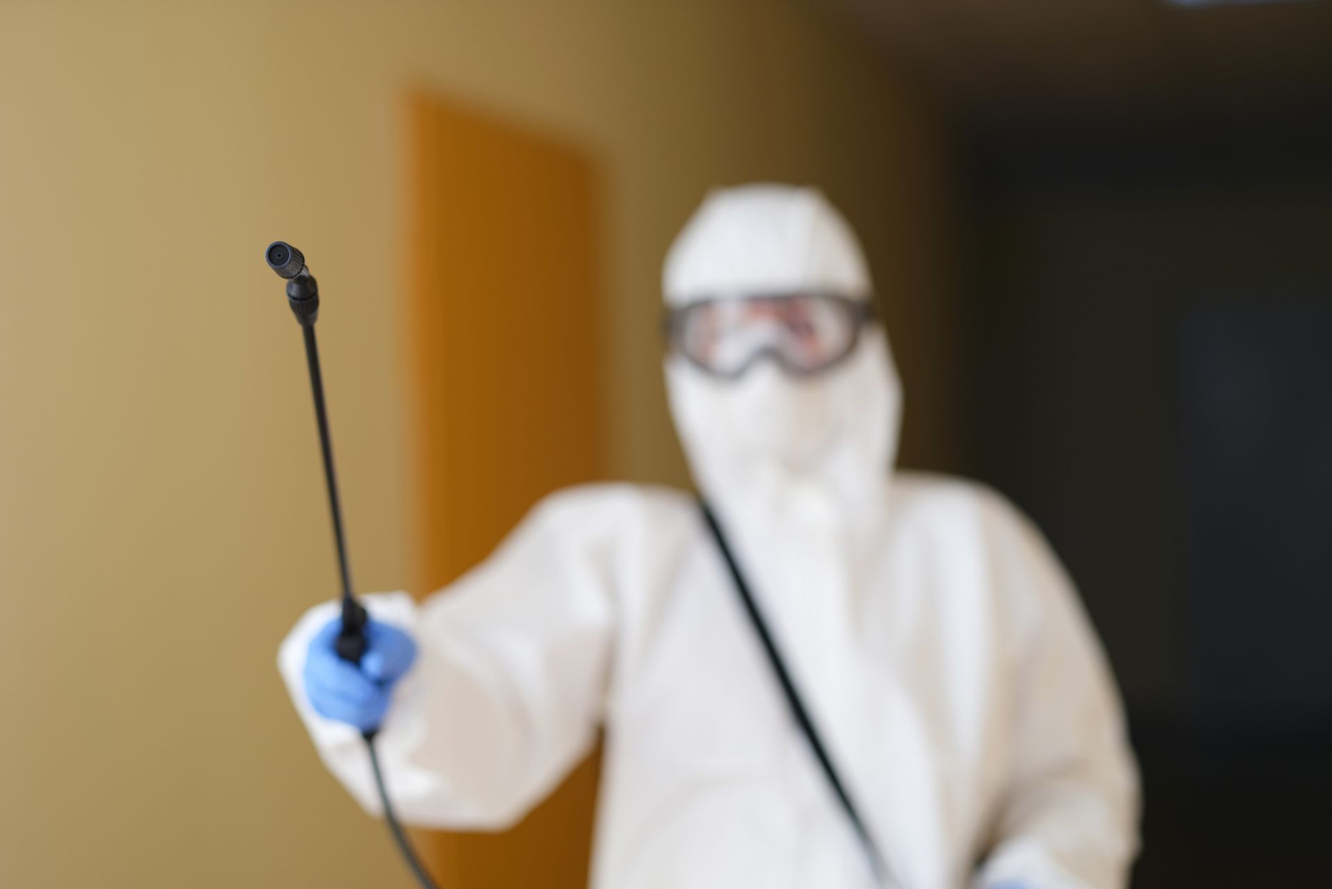 Un uomo con una tuta protettiva sta spruzzando una stanza con uno spruzzatore.