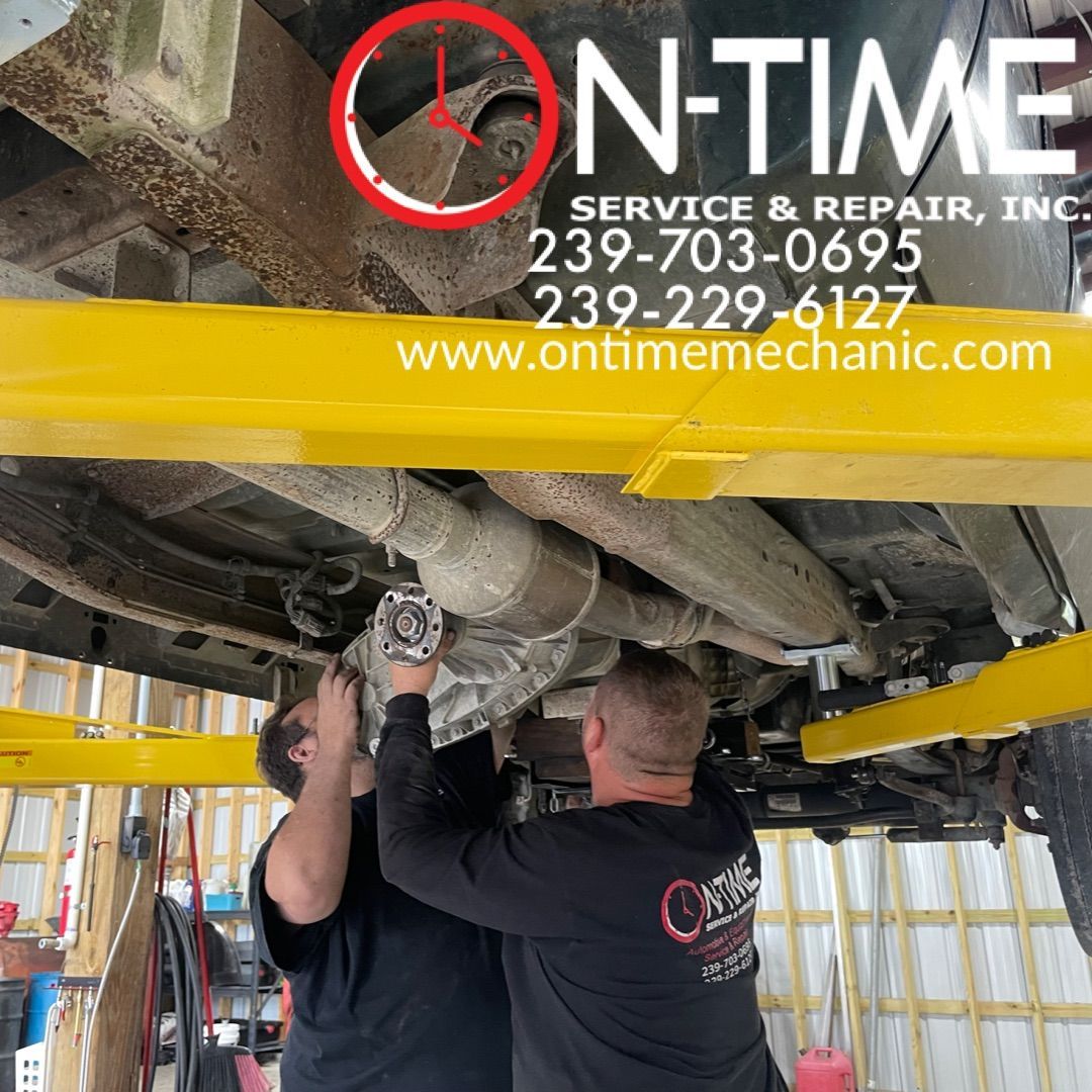 Two men are working underneath a truck with the website www.ontimemechanic.com