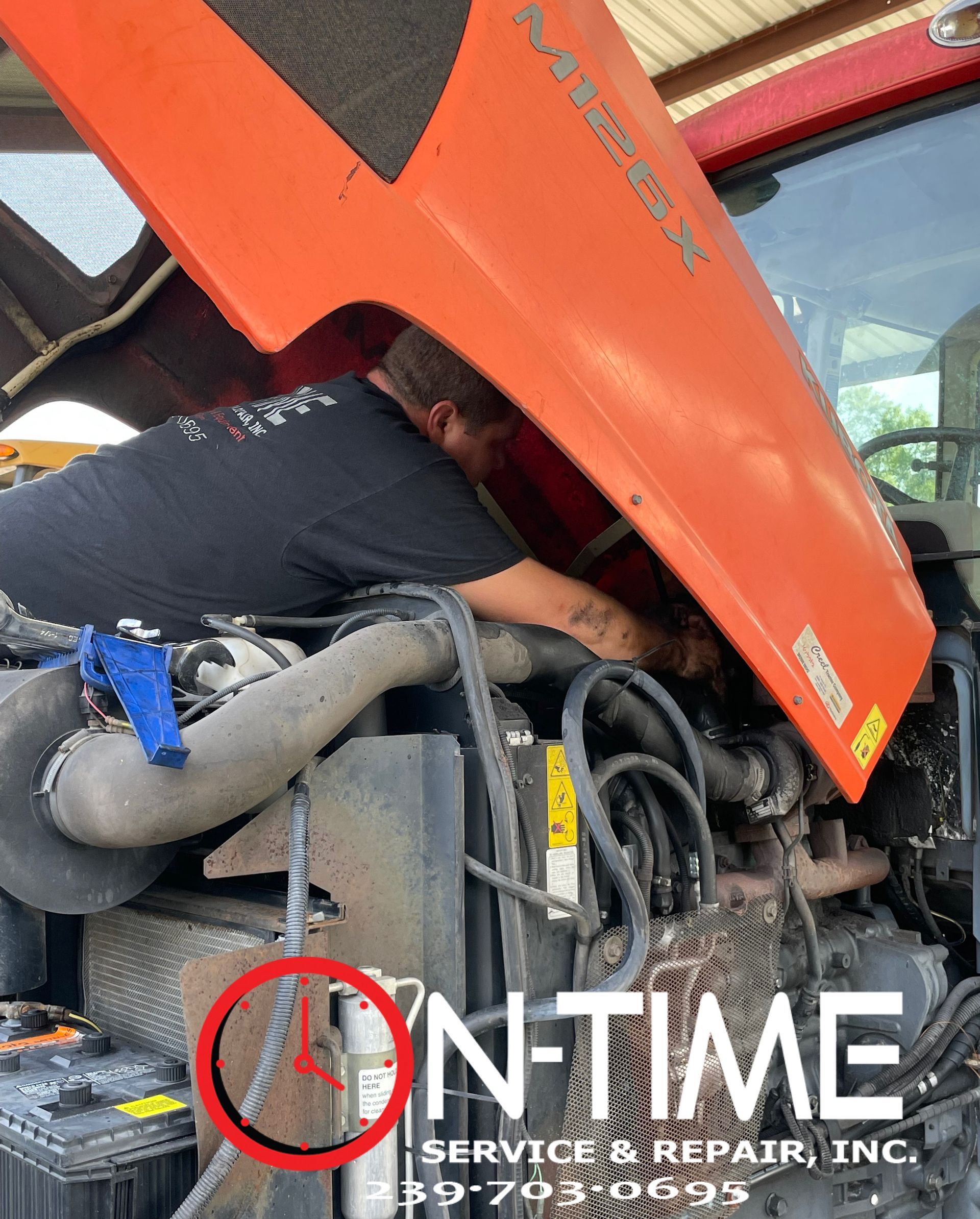 A man is working on the engine of a tractor with the hood up.