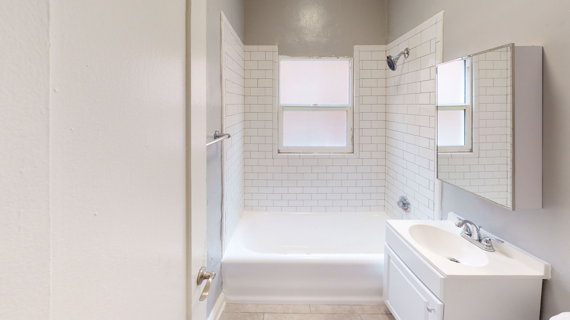 White bathroom with bathtub, subway tile, and a sink with a mirror.
