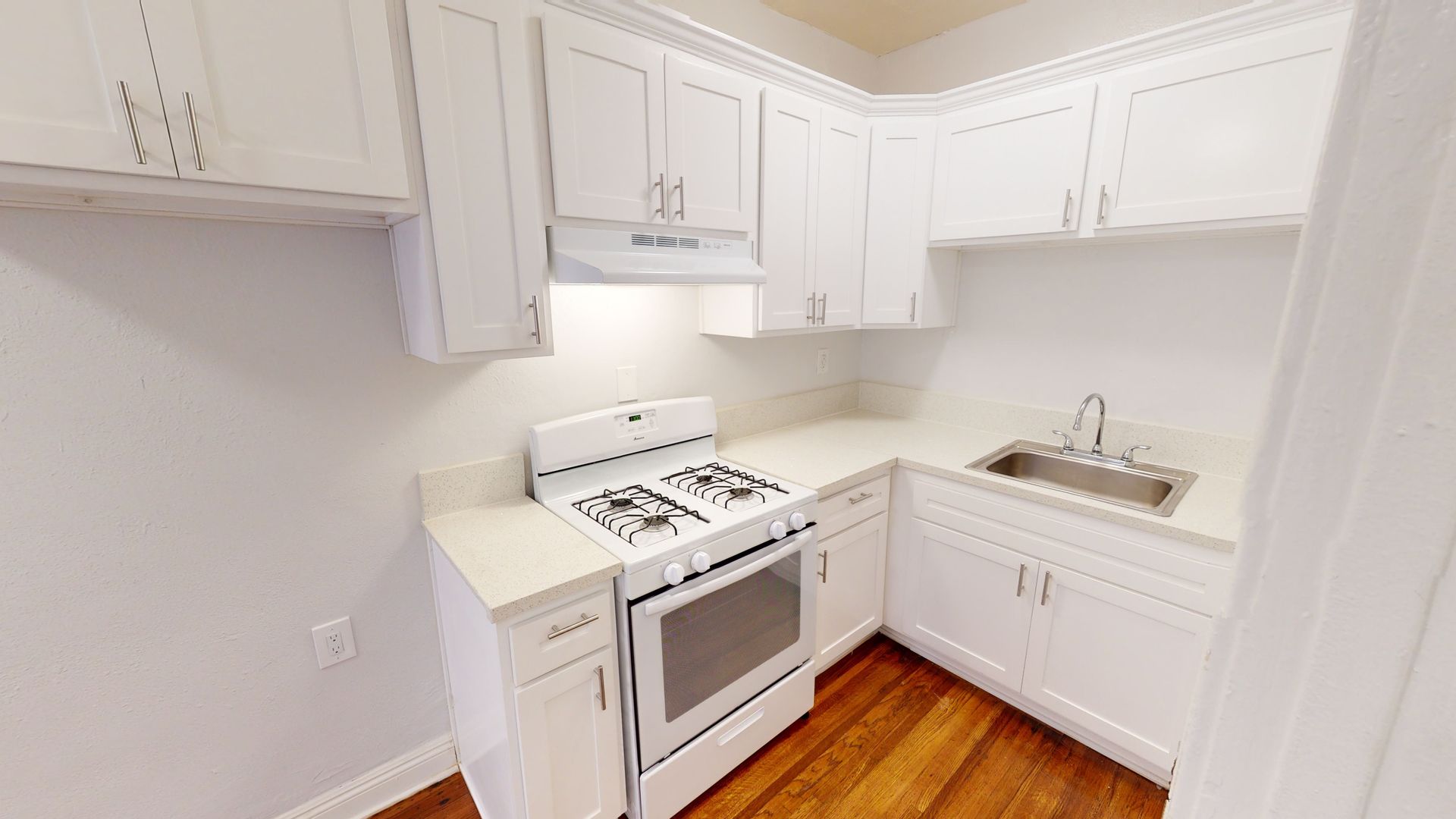 White kitchen with stove, cabinets, sink, and wooden floor.