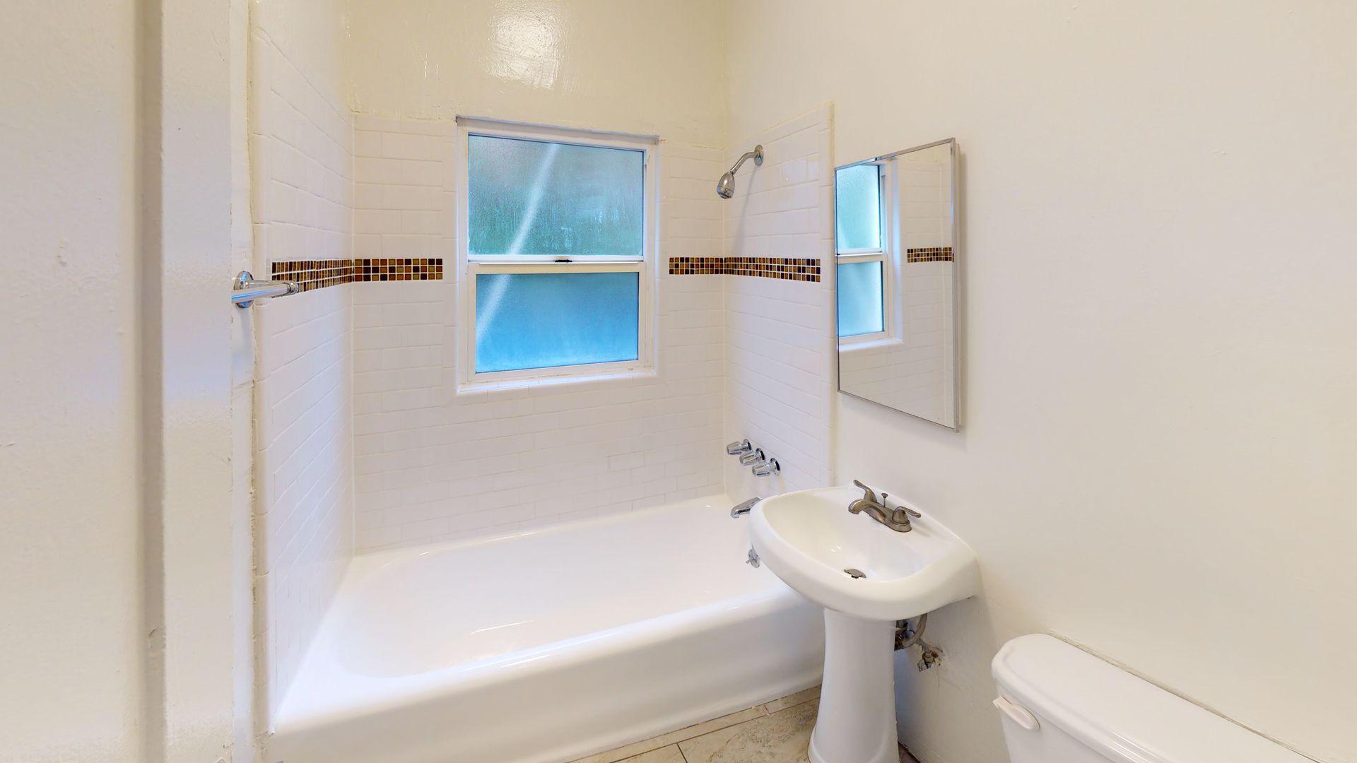 Small, white bathroom with a window, sink, mirror, and toilet; brown tile accents.