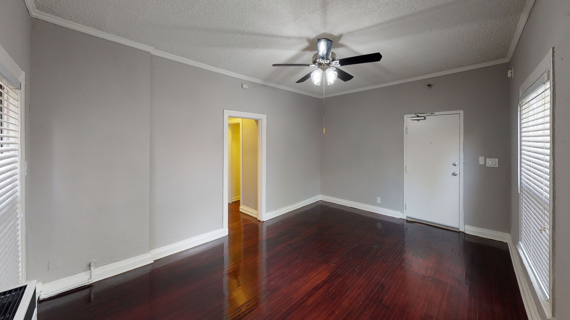Empty living room with wood floors, gray walls, ceiling fan, white trim, and doors.