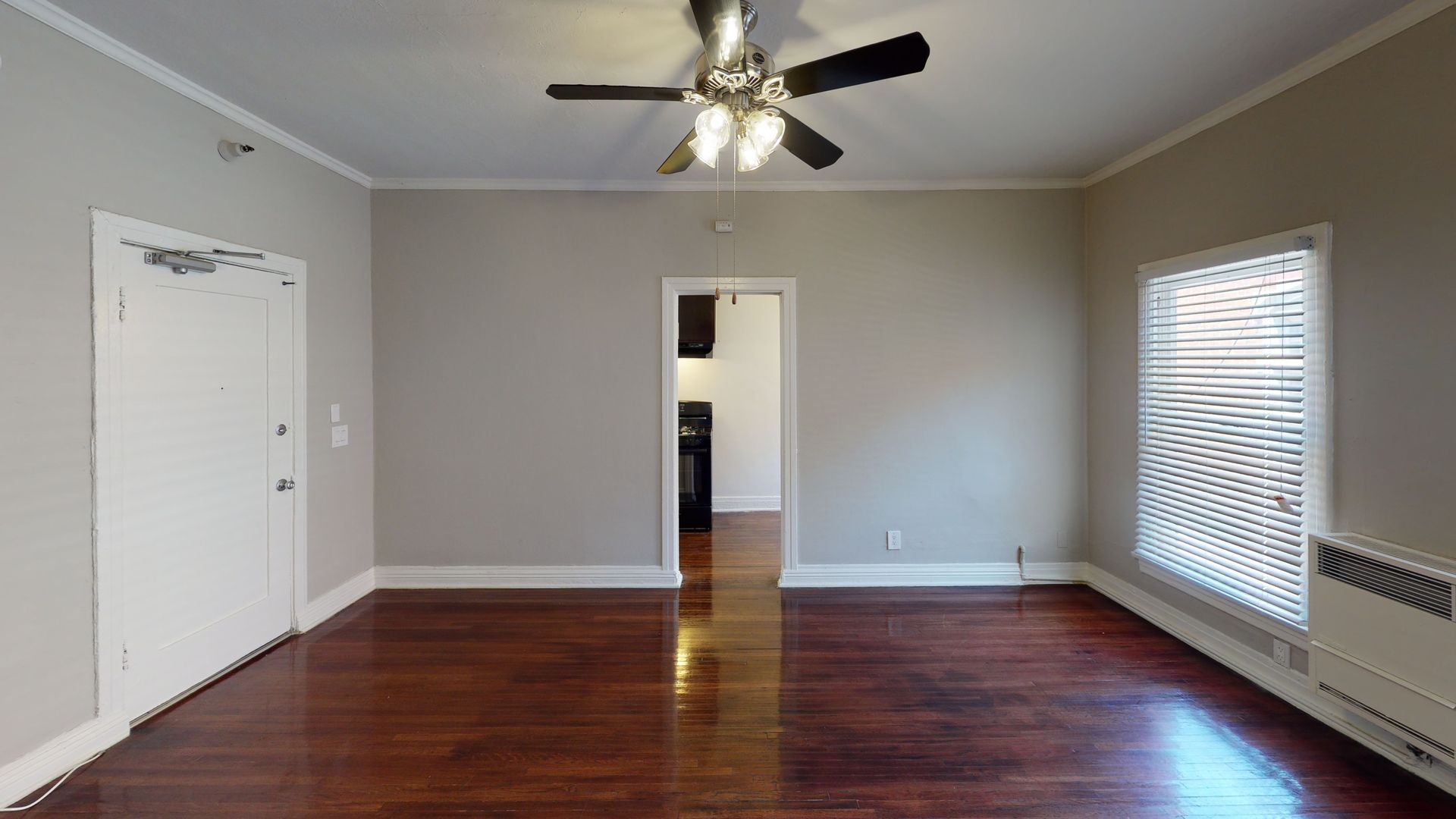 Interior of a room with dark wood floors, light gray walls, white trim, a ceiling fan, and an open doorway.