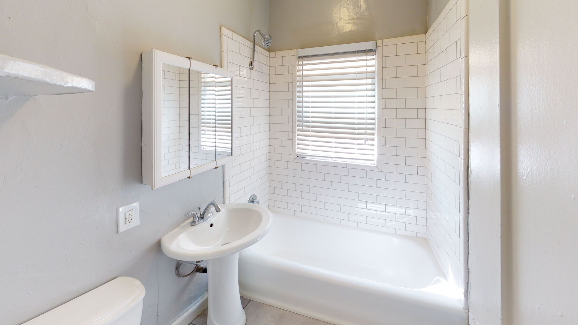 Bathroom with white tile, a bathtub, pedestal sink, and a medicine cabinet.