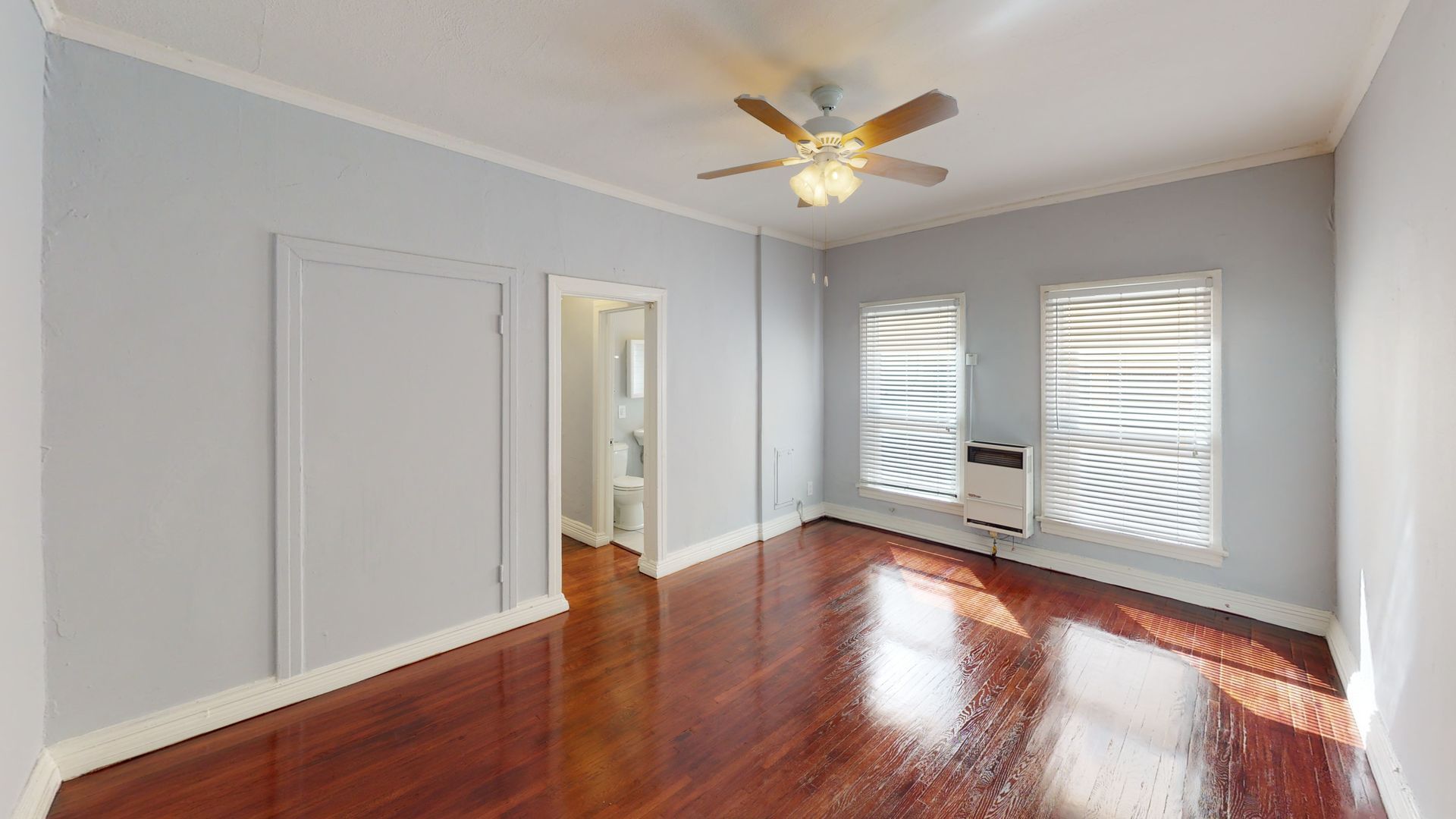 Empty room with hardwood floors, light blue walls, two windows, and a ceiling fan.