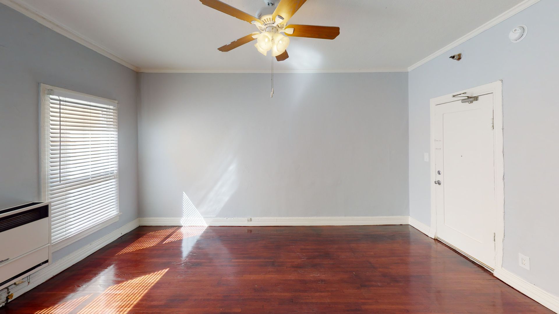 Empty room with hardwood floors, a ceiling fan, and a window letting in sunlight.