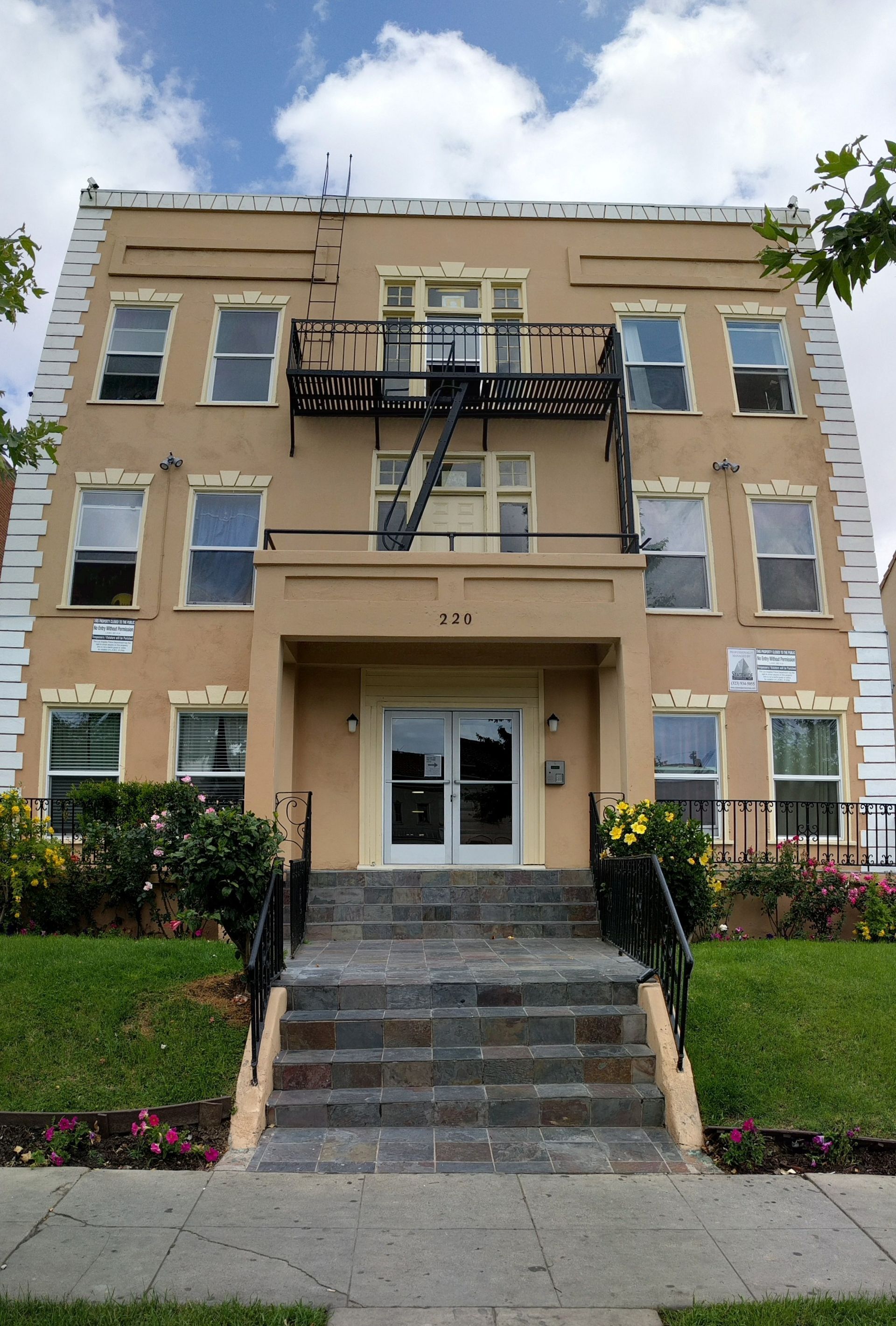 Beige three-story building with a black fire escape, stone steps, and a double-door entrance.