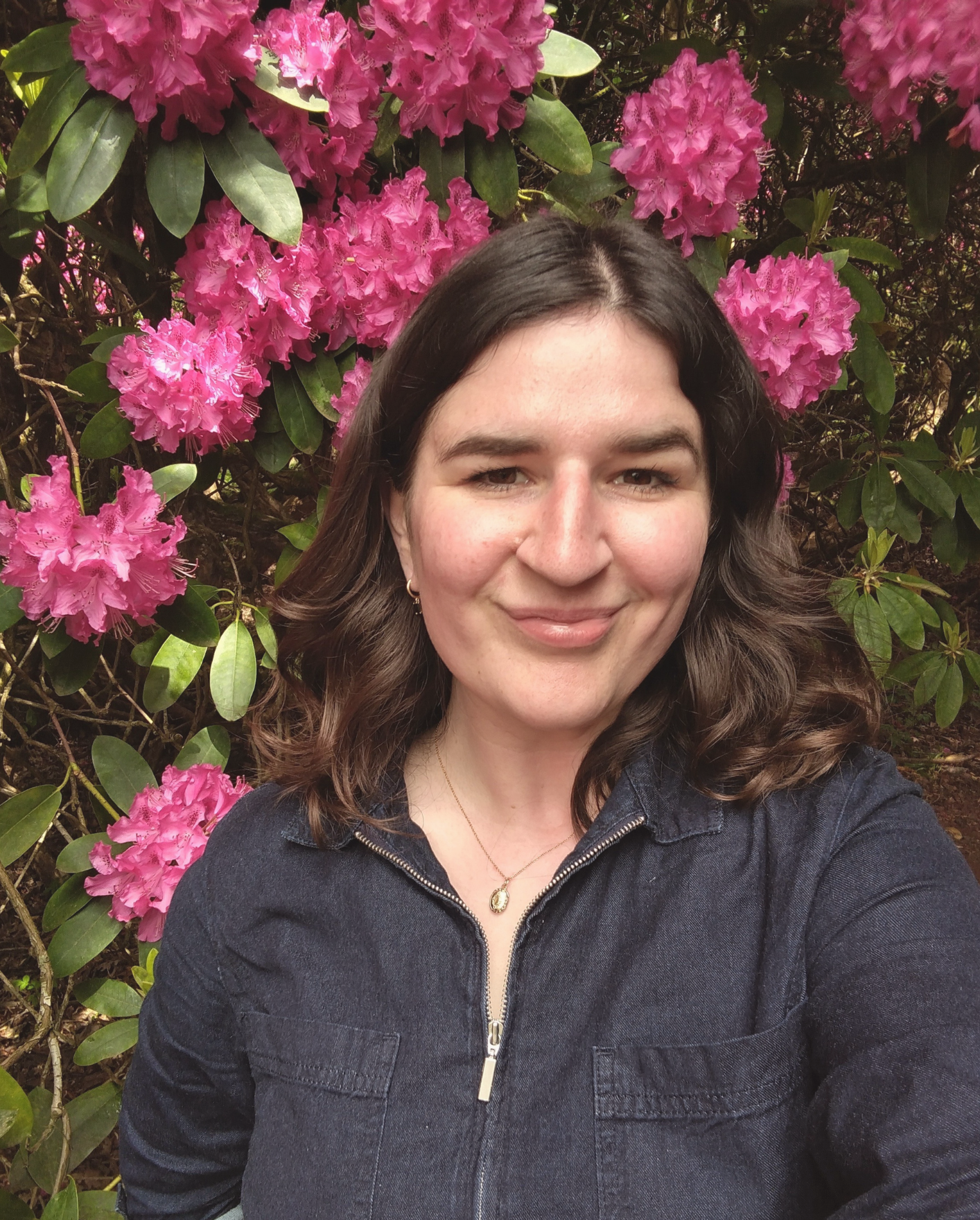 Lucy Newport is smiling in front of a bush of pink flowers.