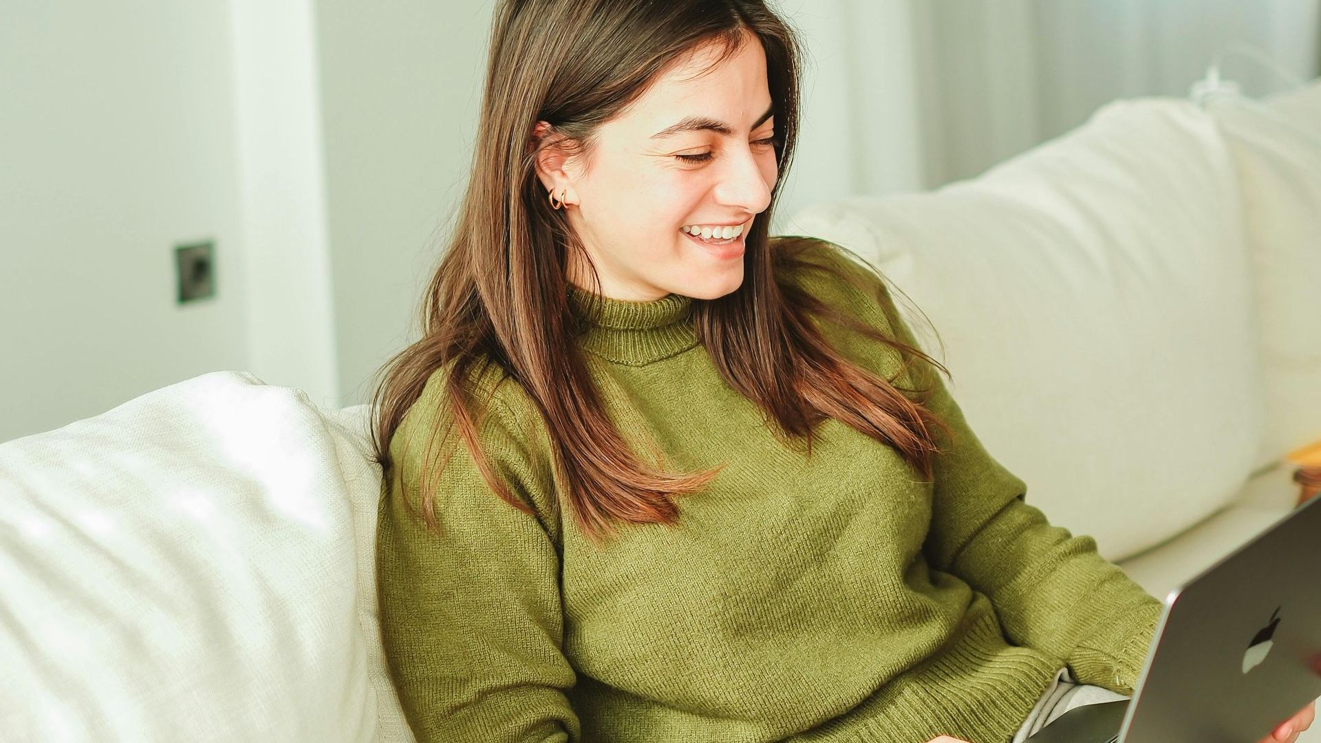 A woman is sitting on a couch using a laptop computer.