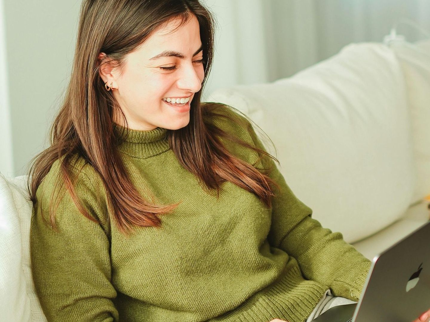 A woman is sitting on a couch using a laptop computer.