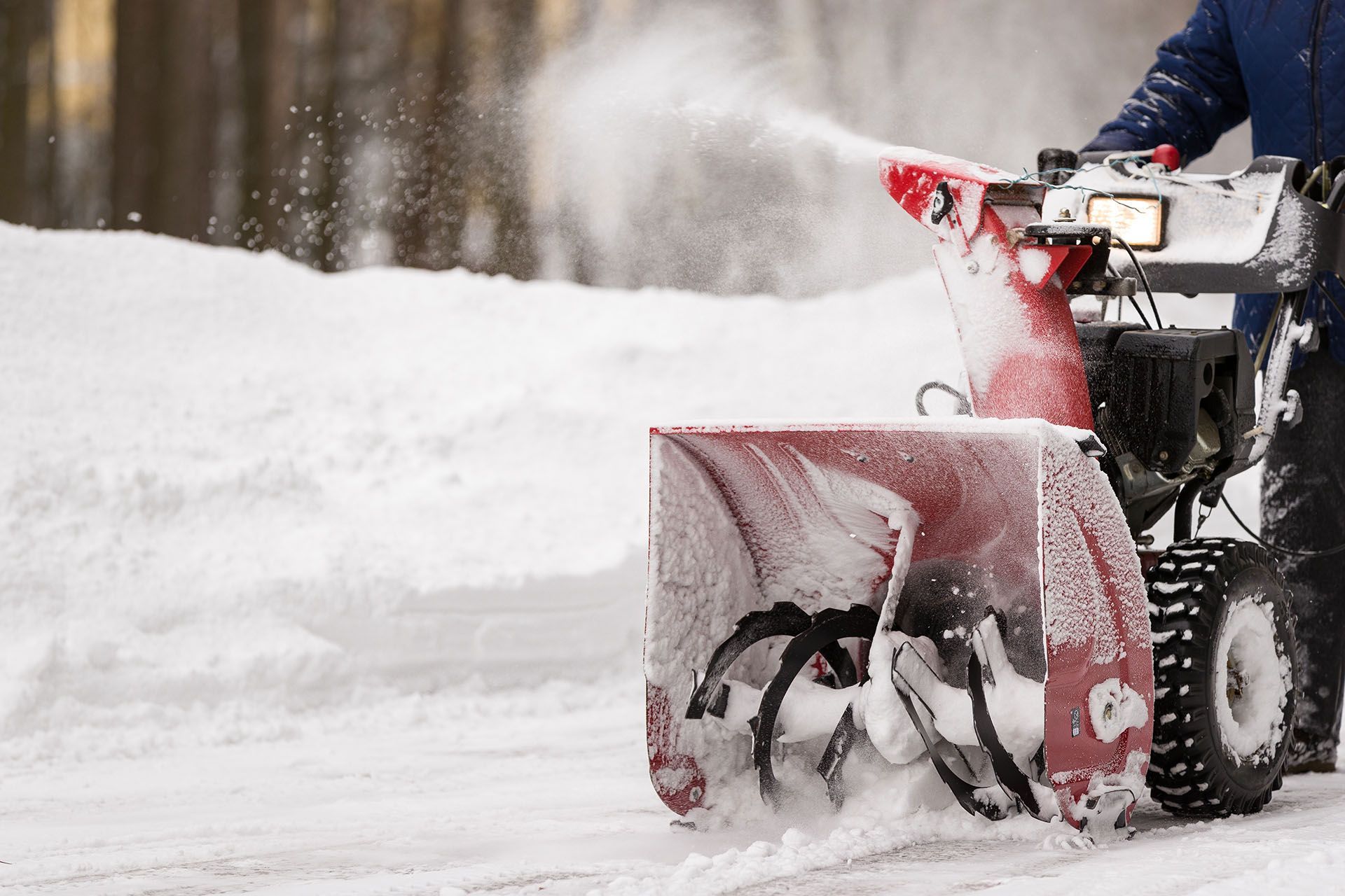 Person using a red snowblower to clear snow from a paved surface