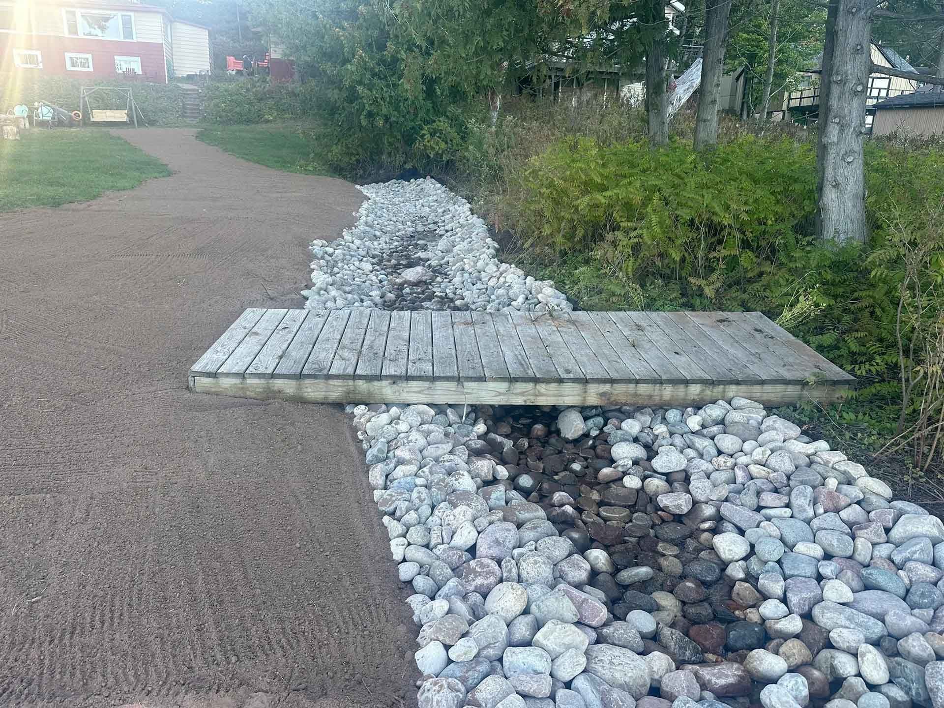 Wooden bridge over a small rock-lined stream with a gravel path on either side
