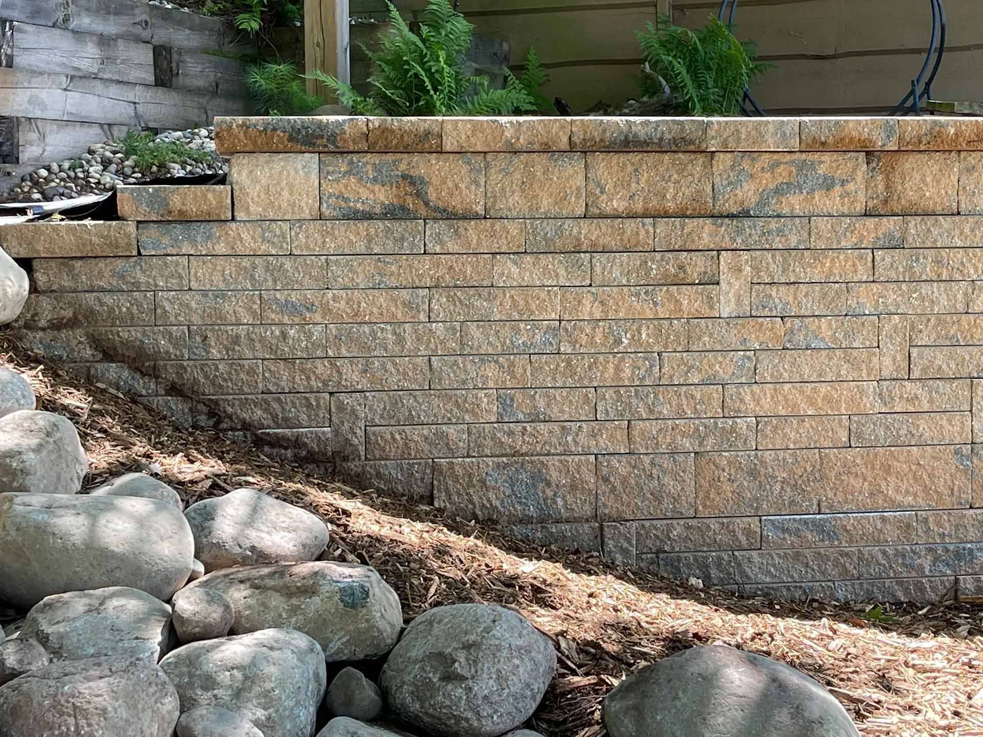 Stone retaining wall with a planter box, rocks, and foliage
