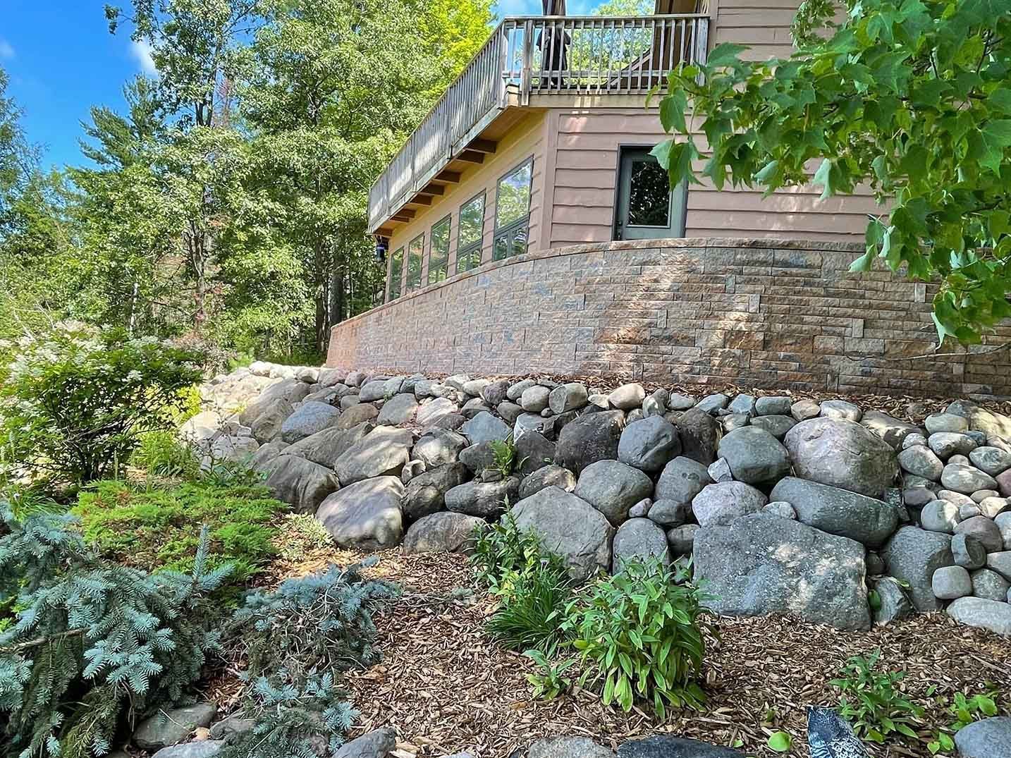 A stone retaining wall supports a building with a balcony overlooking a lake