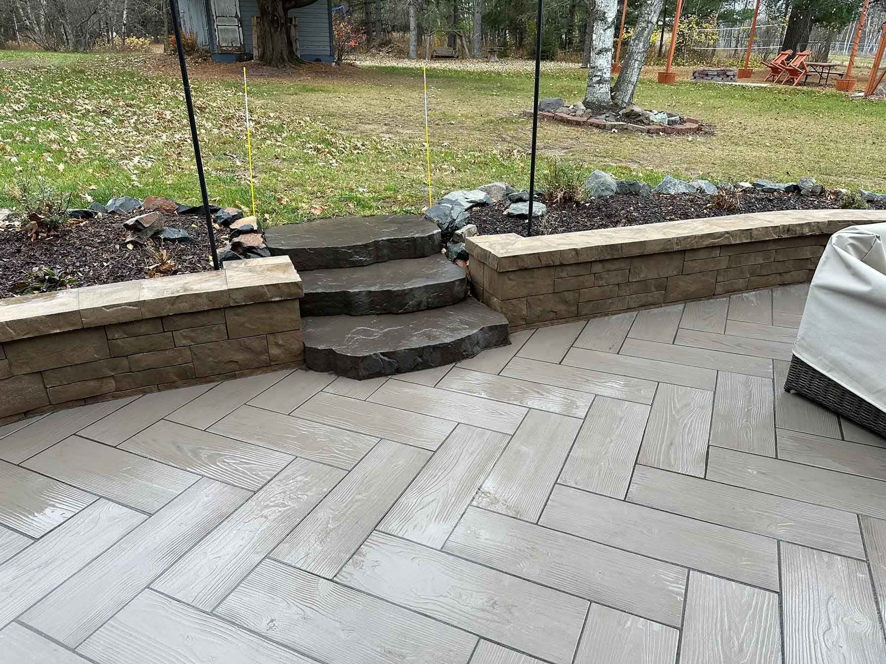 Outdoor patio with stone steps leading to a raised garden bed and green lawn