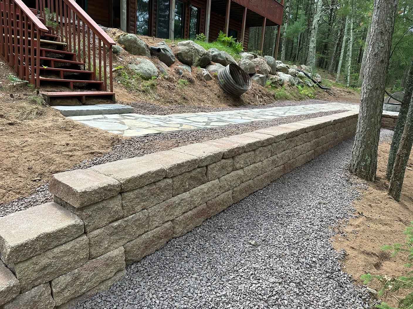 A retaining wall made of tan blocks beside a gravel path leading to a house