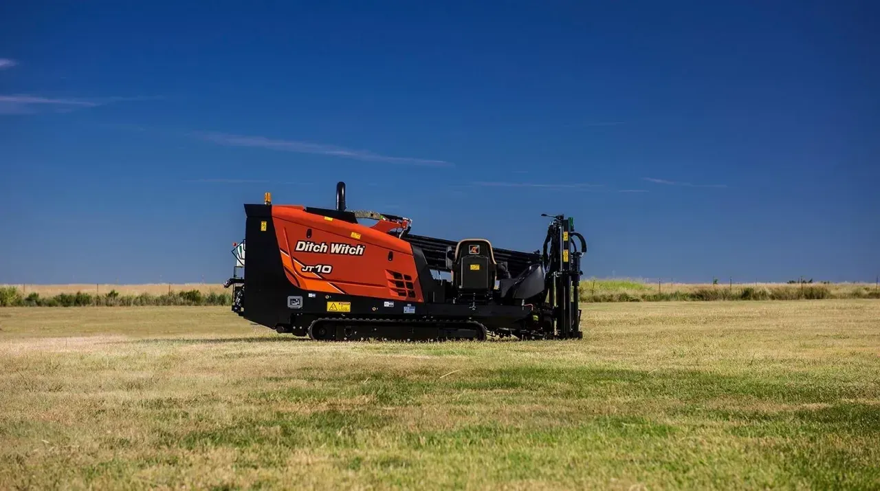 Orange trencher machine in a field under a blue sky