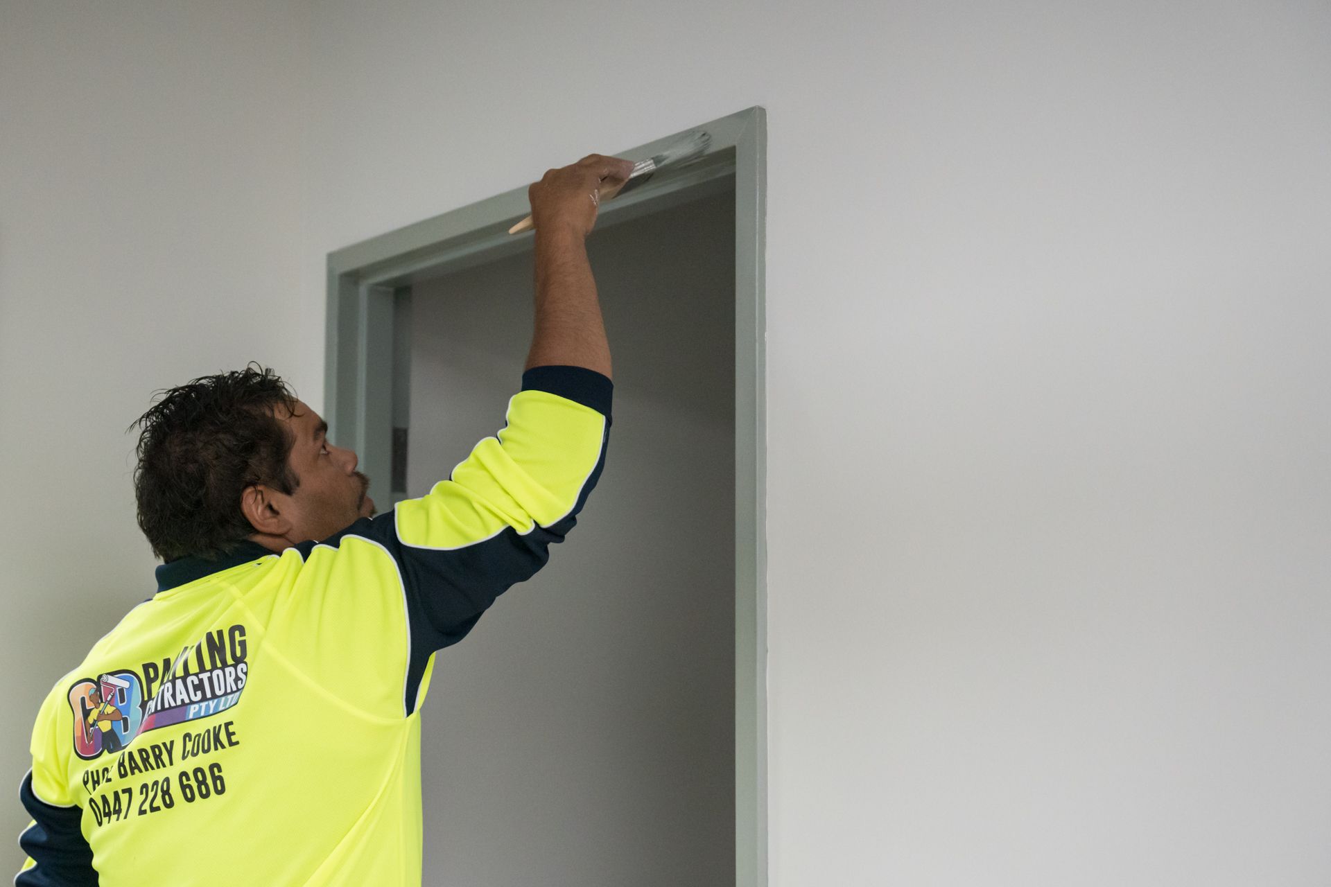 A man in a yellow shirt is painting a door frame.
