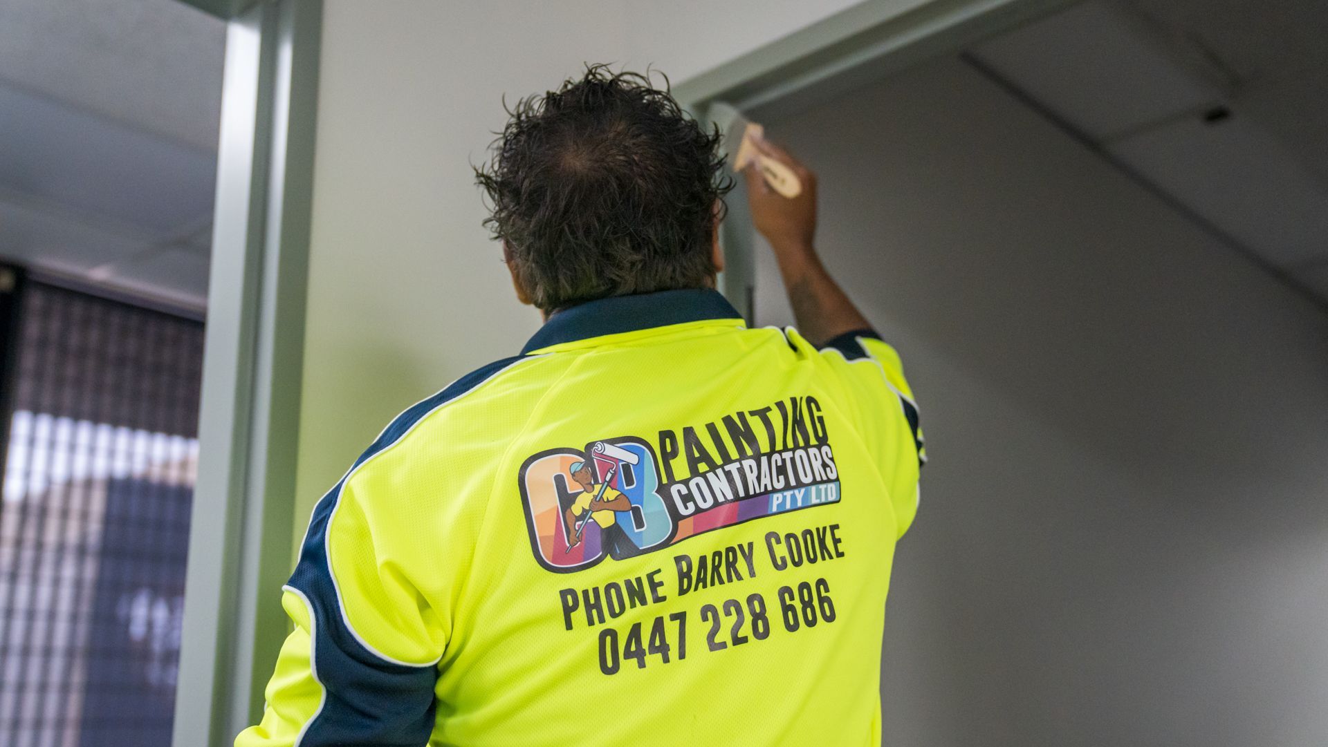 A man wearing a painting contractor shirt is painting a wall.