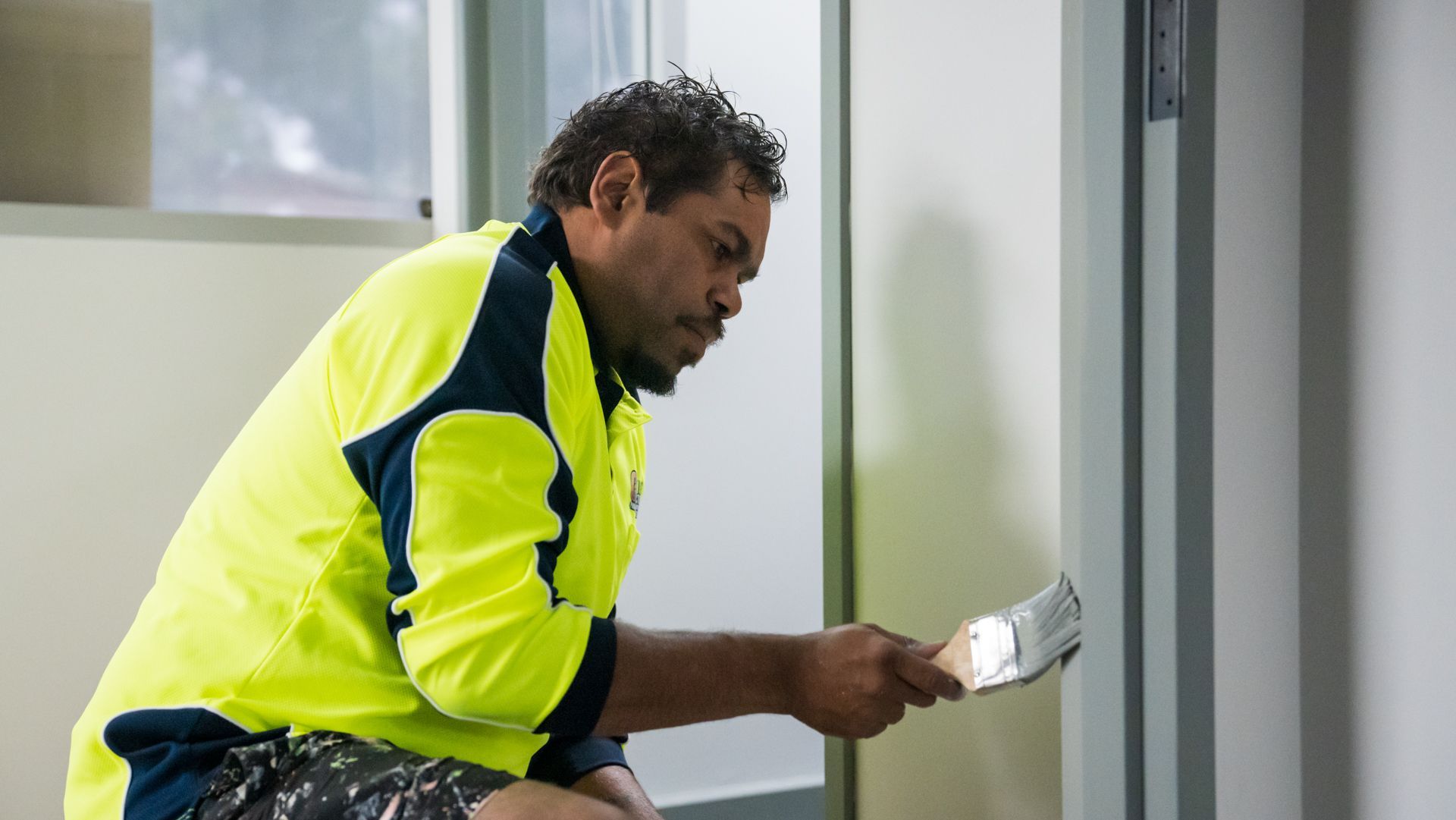 A man is sitting on the floor painting a wall with a brush.