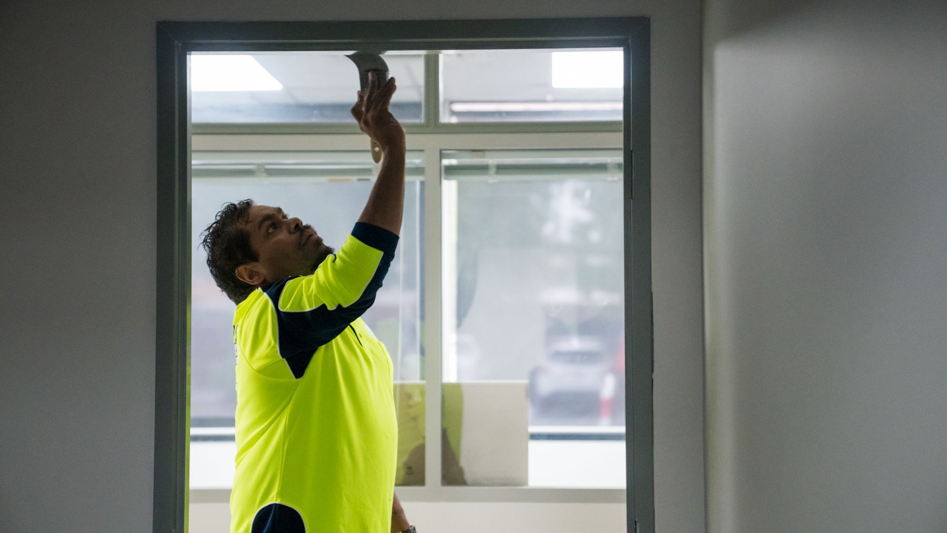A man in a yellow shirt is working on a window frame.