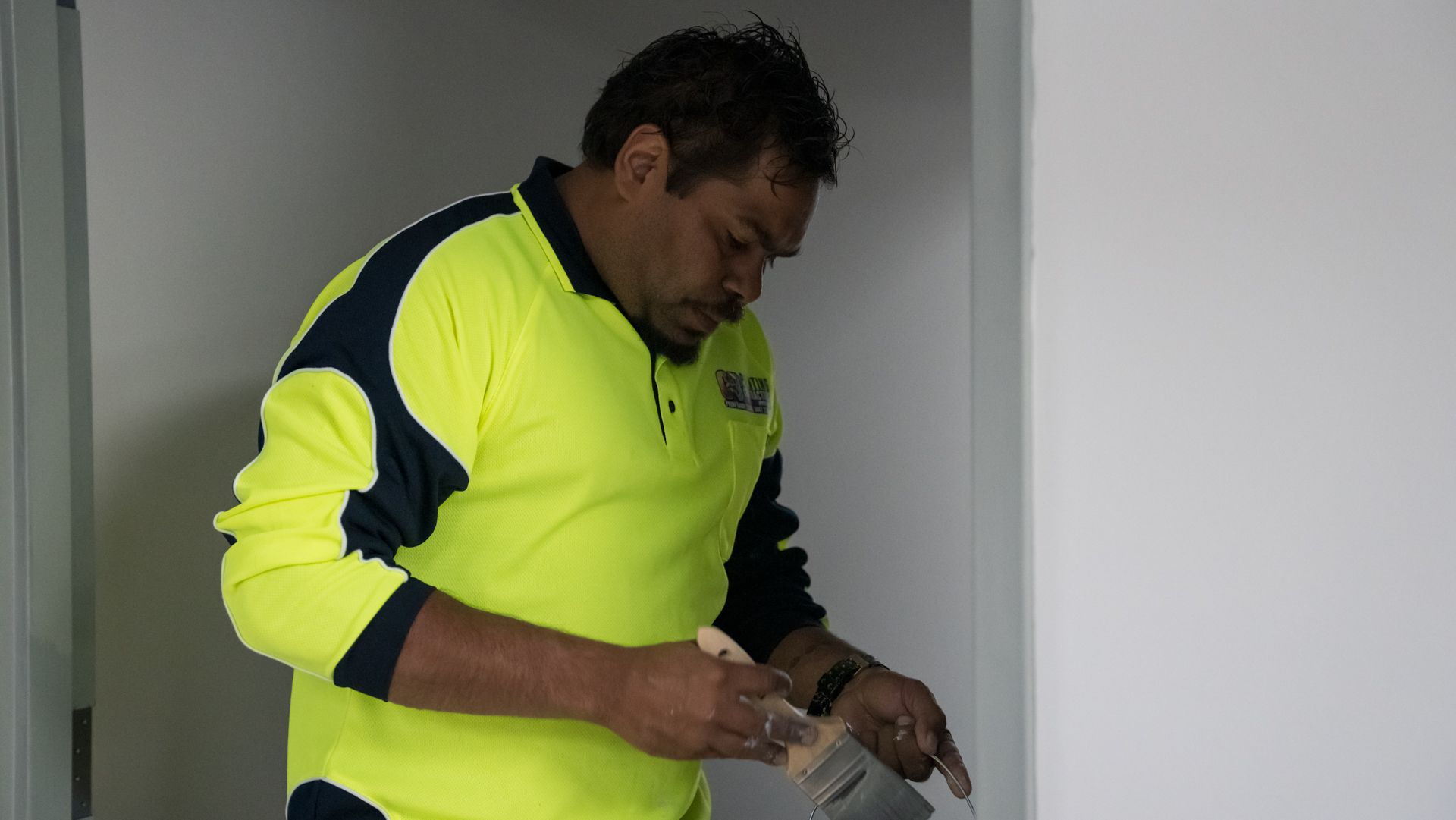 A man in a neon yellow shirt is painting a wall with a brush.