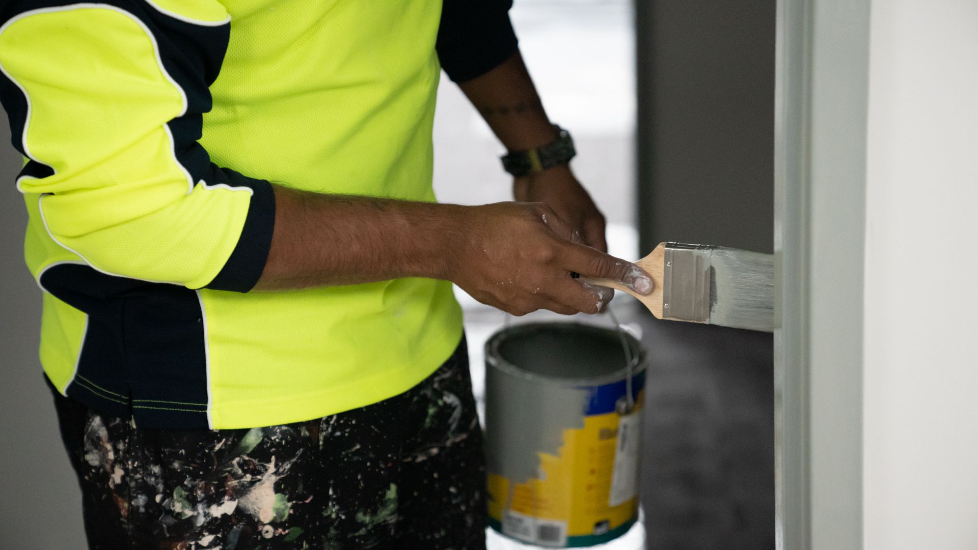 A man is painting a wall with a brush and a can of paint.