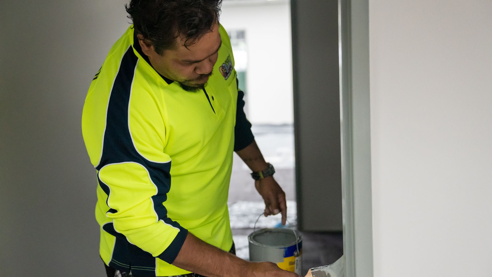 A man in a neon yellow shirt is painting a wall.