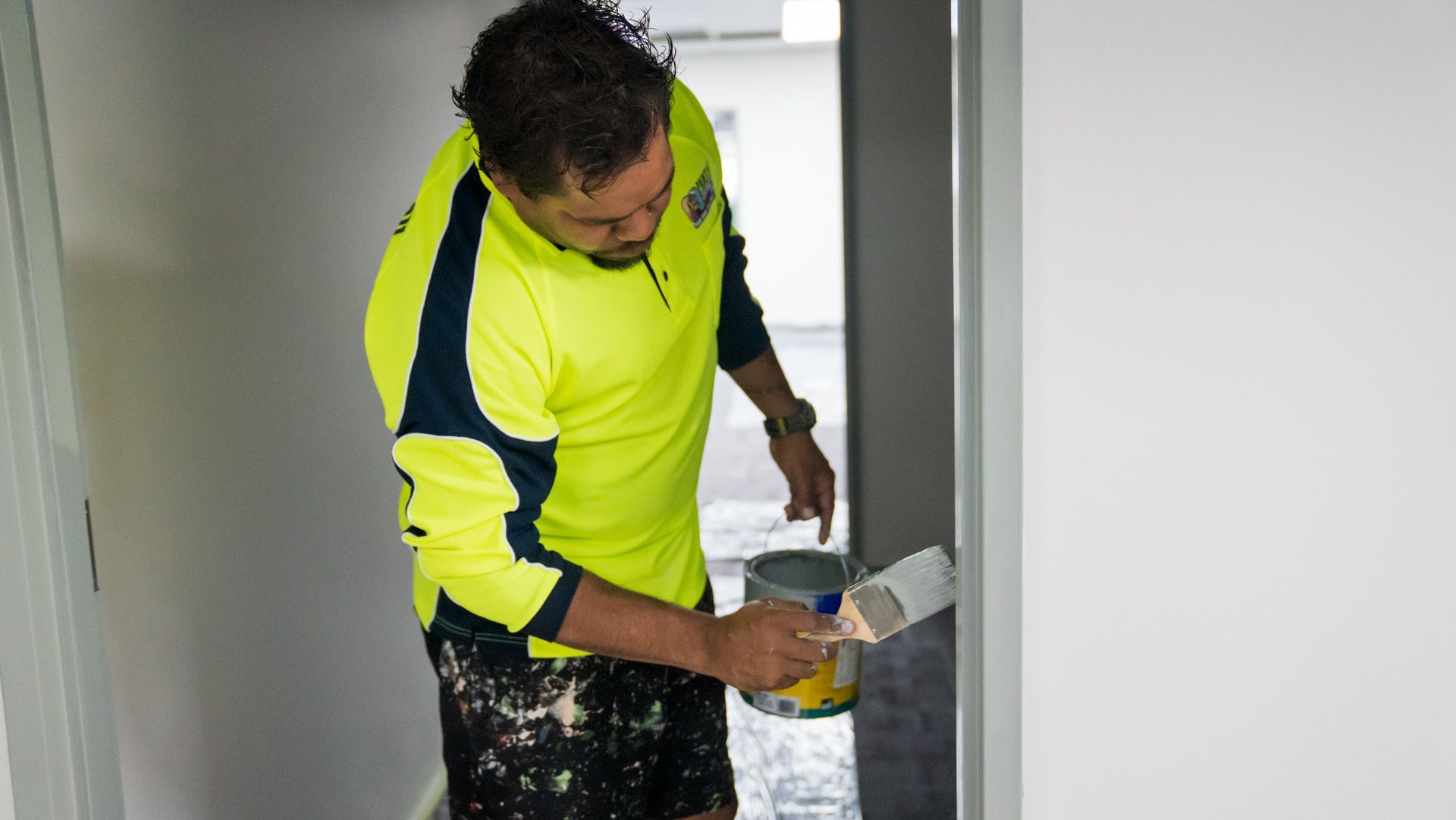 A man is painting a wall with a brush and a can of paint.