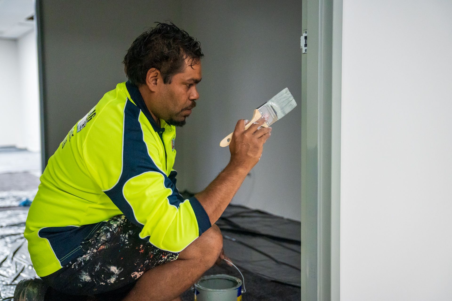 A man is kneeling down and painting a door with a brush.