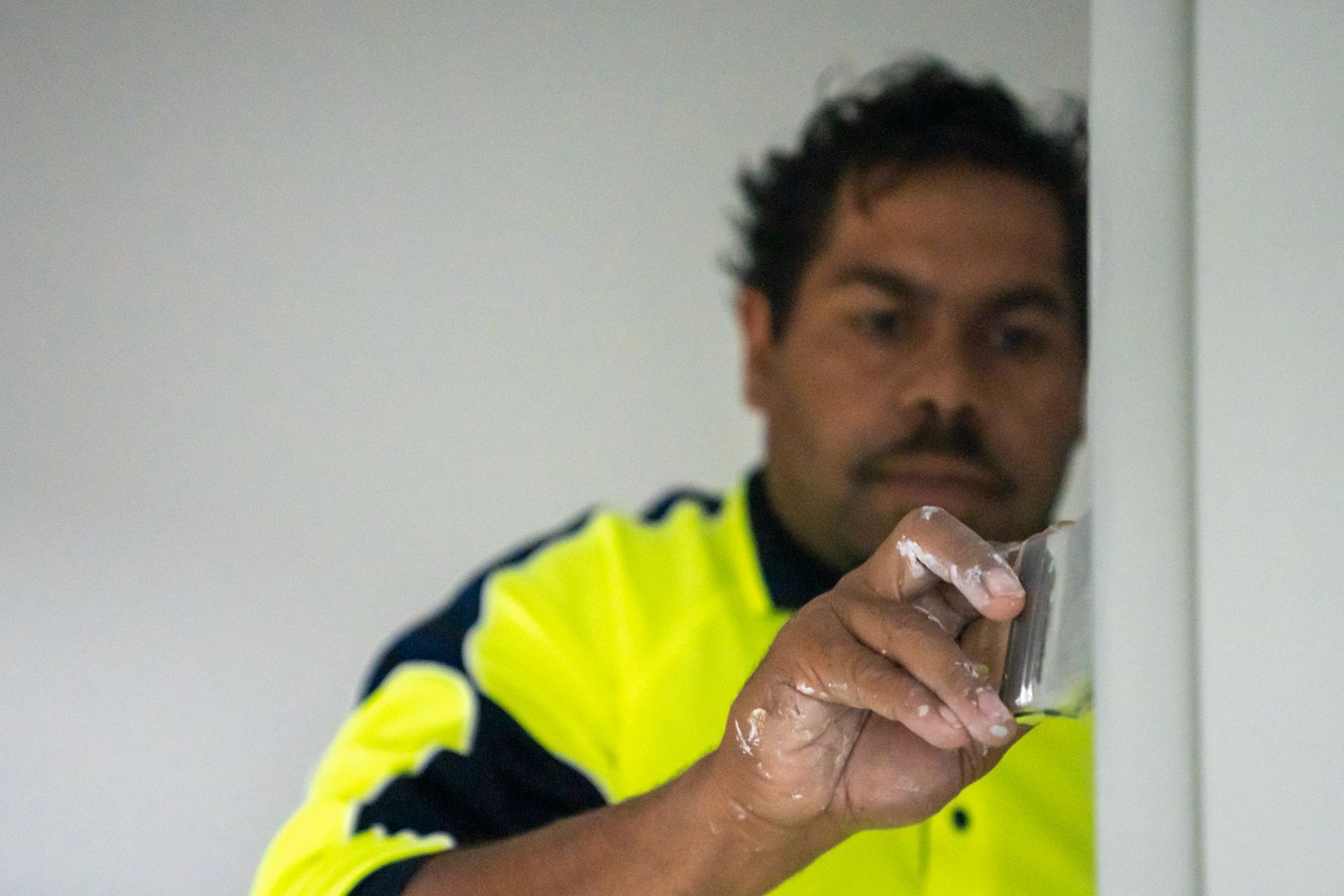 A man in a yellow and blue shirt is painting a wall.