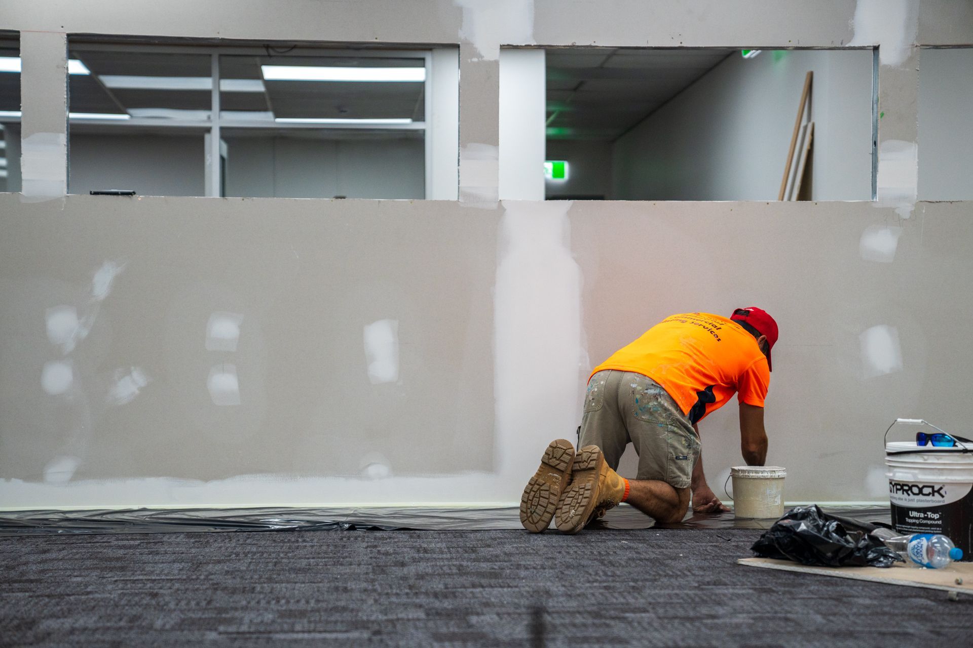 A man in an orange shirt is kneeling on the floor.