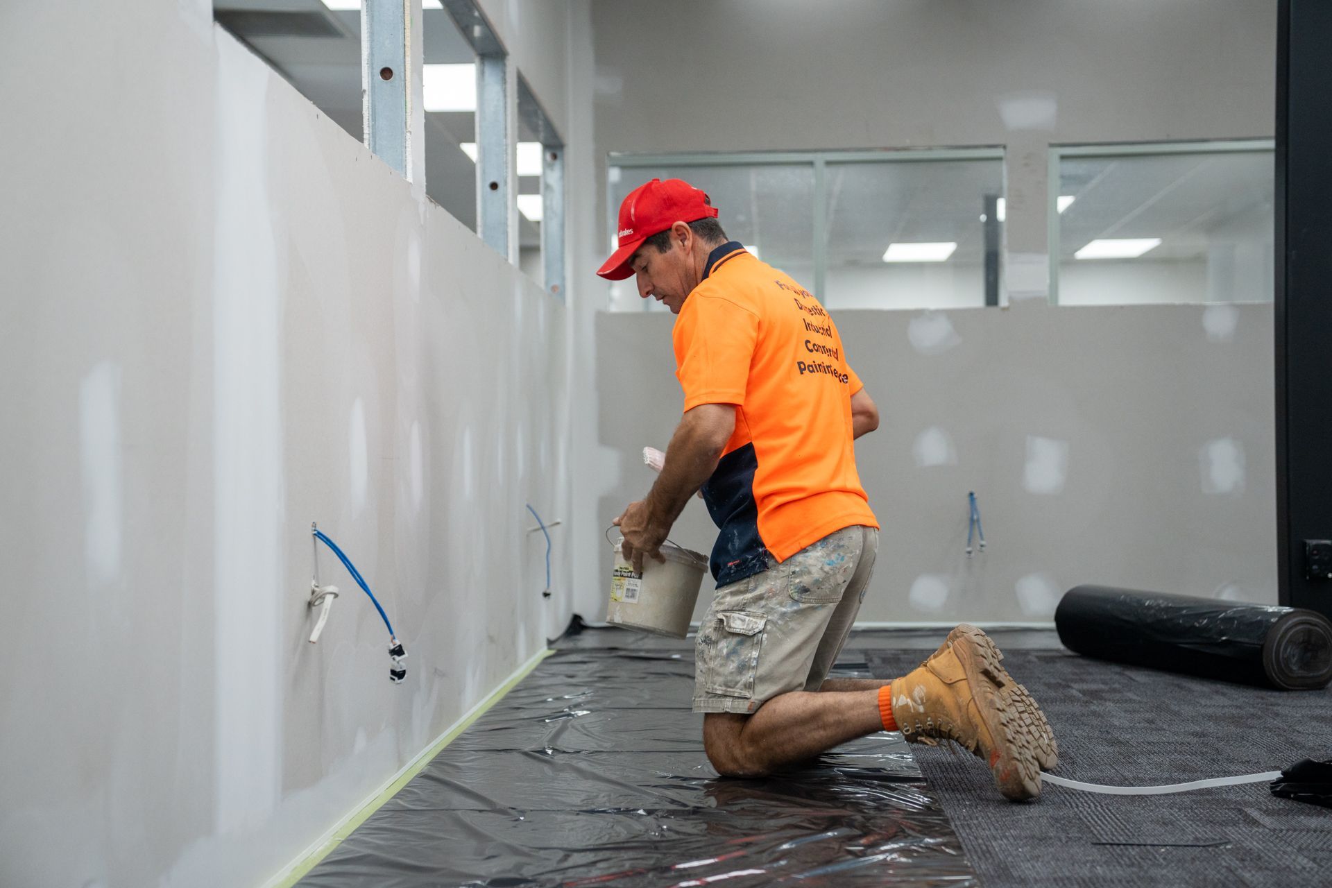 A man is kneeling on the floor while painting a wall.