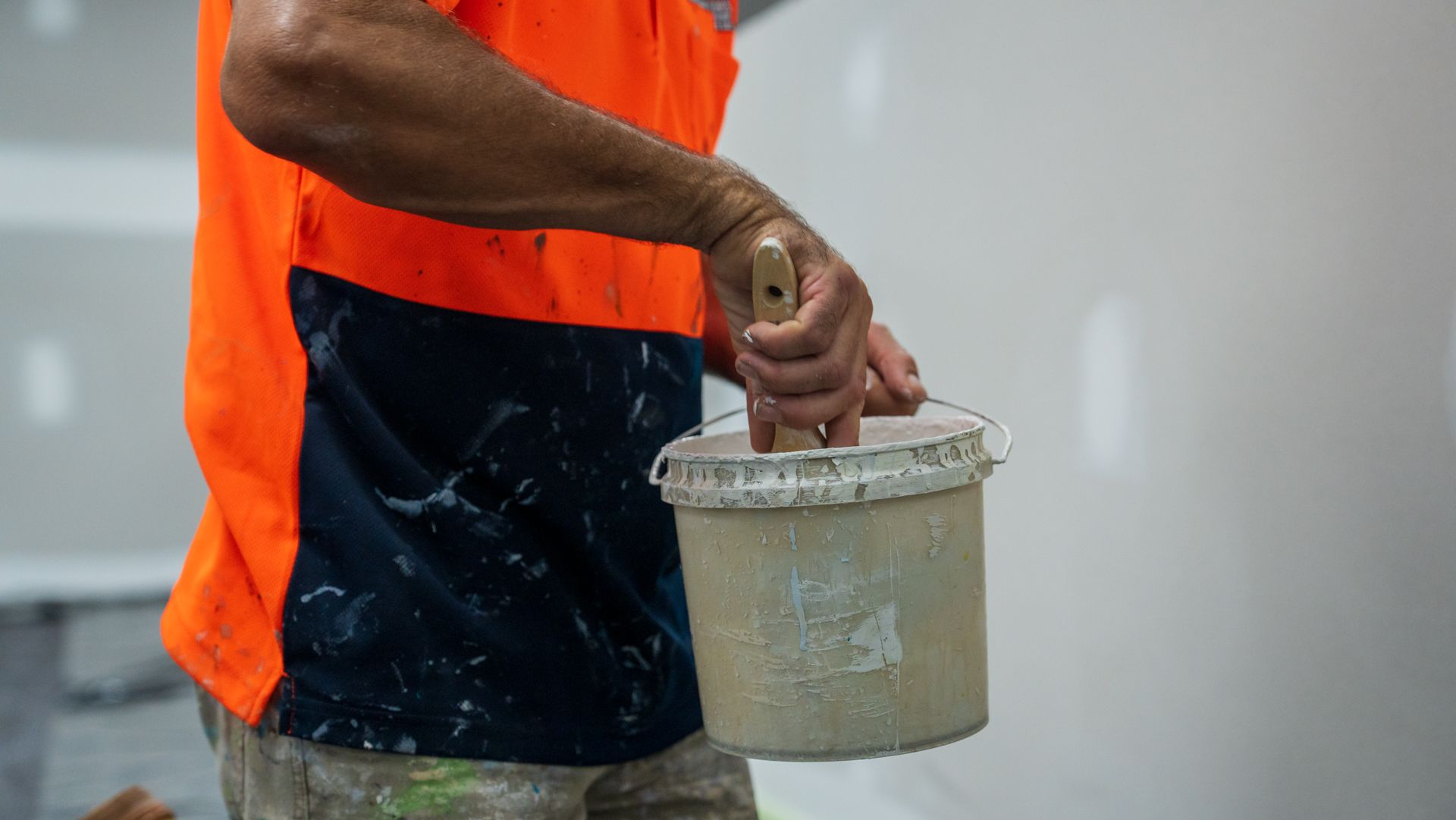 A man is holding a bucket of plaster and a spatula.